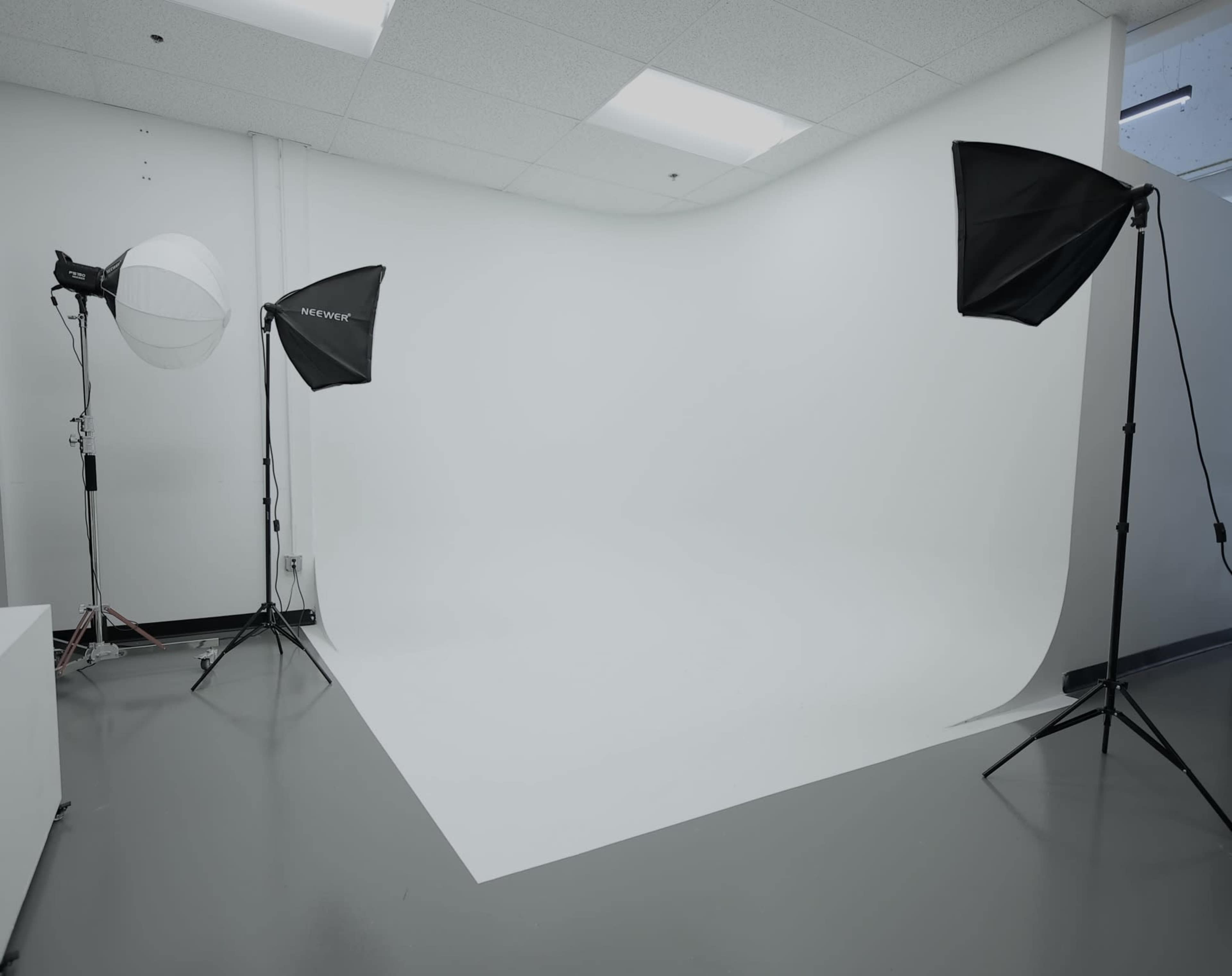 The image shows a photography studio featuring a seamless white backdrop, two softbox lights, and a round light diffuser on a stand.