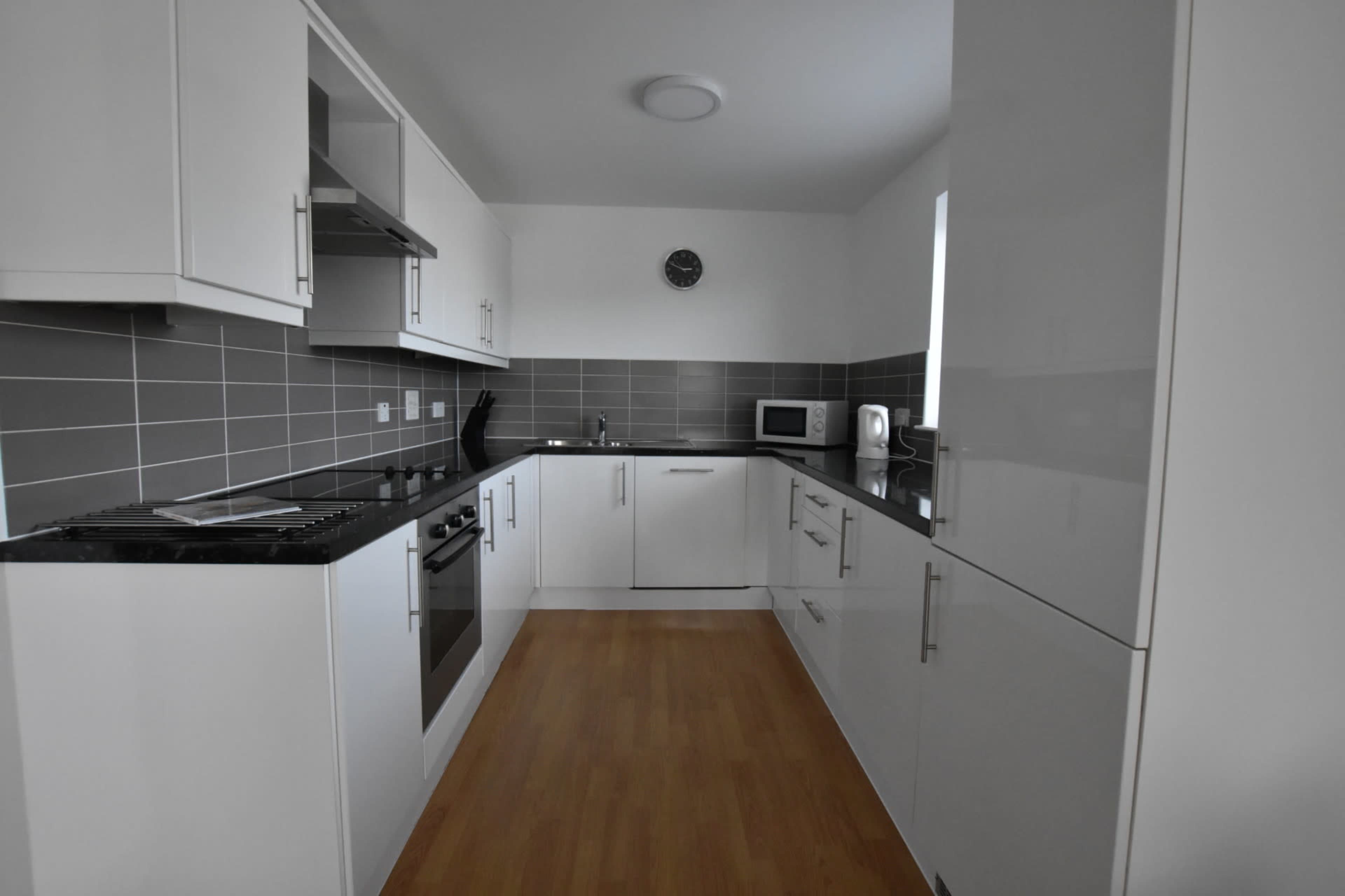 A modern kitchen with white cabinetry, gray tile backsplash, and a wooden floor.