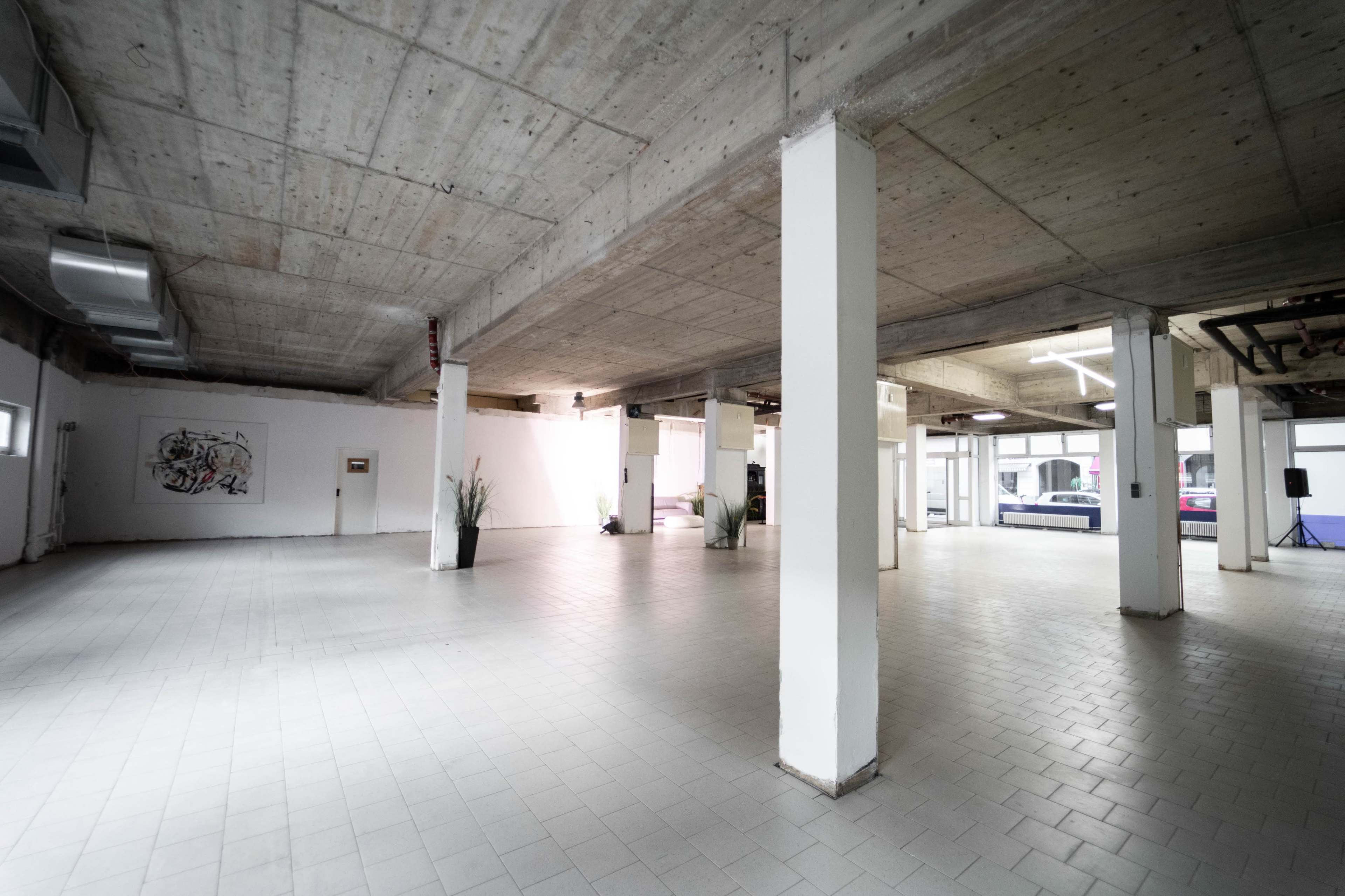 A spacious, empty interior with concrete ceilings and tile flooring, featuring several pillars and minimal decorative elements.