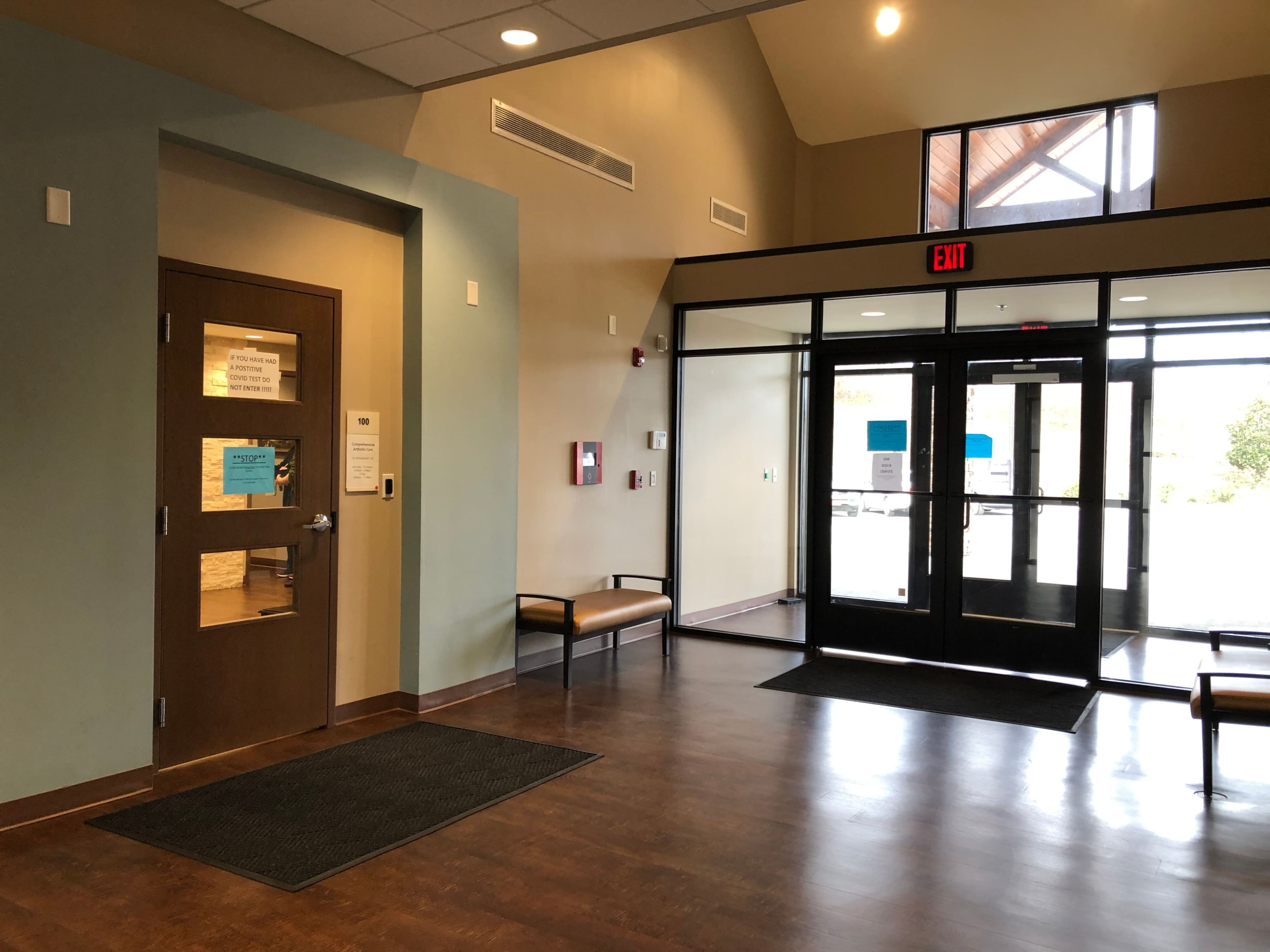 An interior entrance area with a door on the left, benches along the wall, and large glass doors leading outside on the right.
