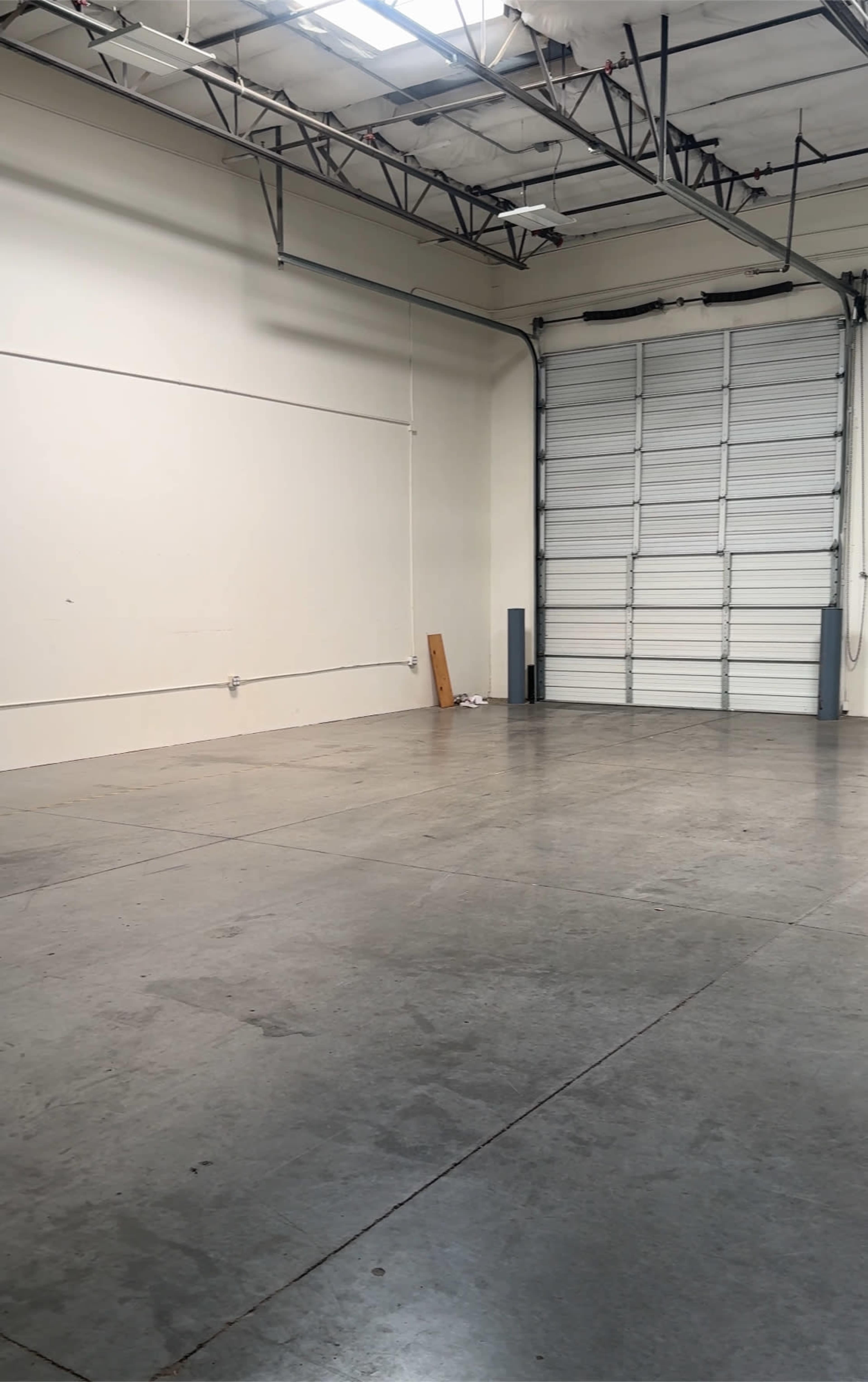 The image shows an empty warehouse space with a concrete floor and a large rolled-up door at one end.