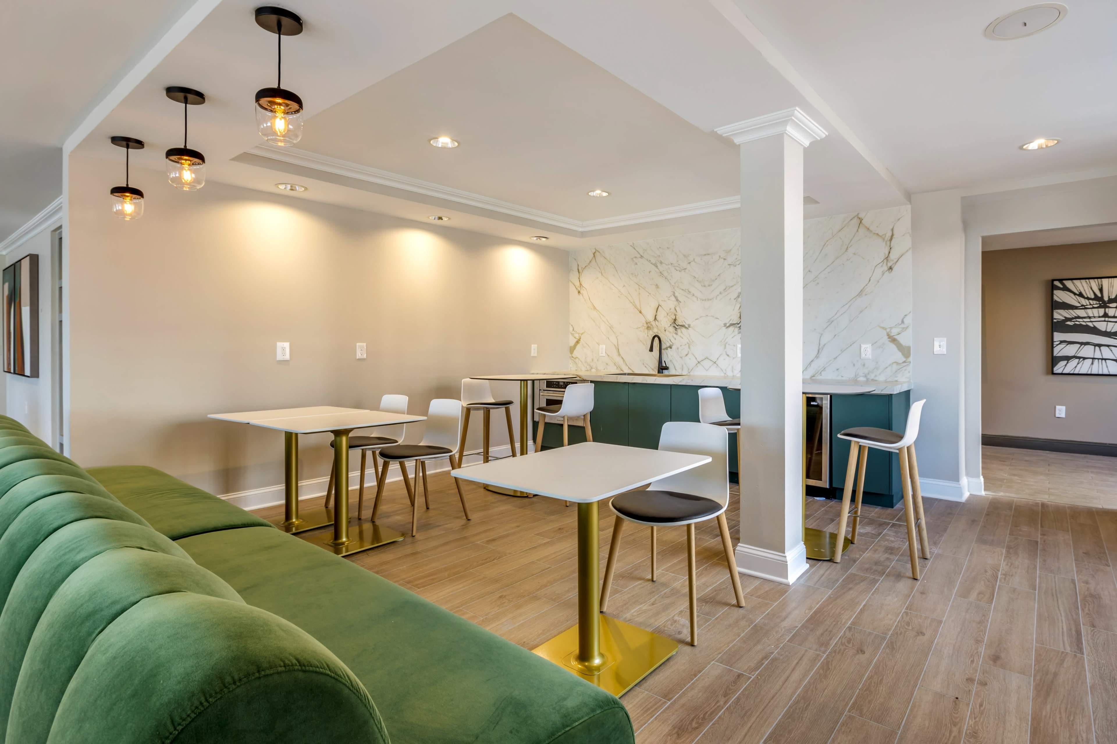 A modern, minimalistic lounge area with green seating, two tables, and a kitchenette featuring marble accents.