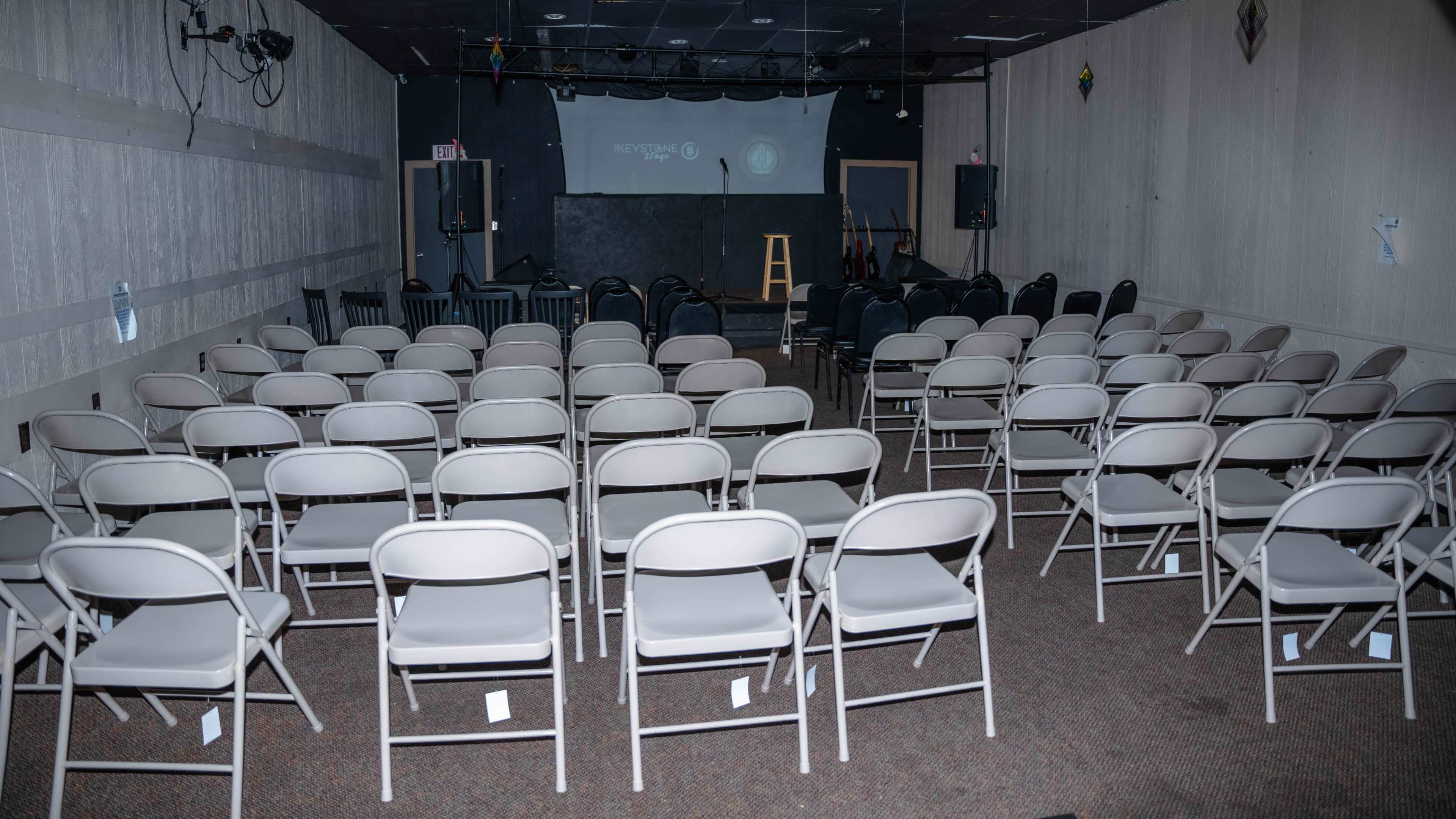 An empty performance space set up with rows of white folding chairs facing a small stage.