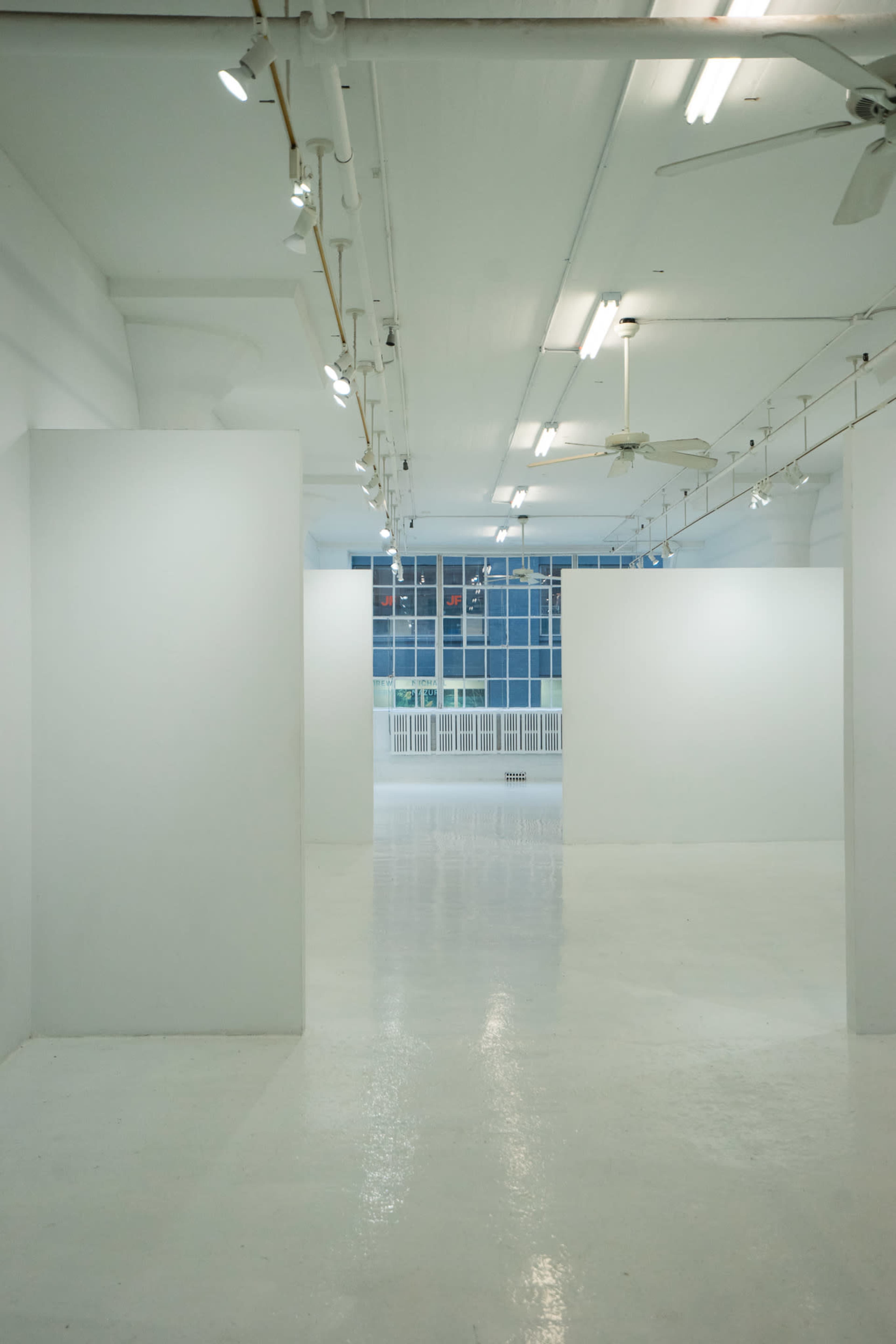 A spacious, minimalist gallery with white walls and polished flooring, illuminated by overhead lights.