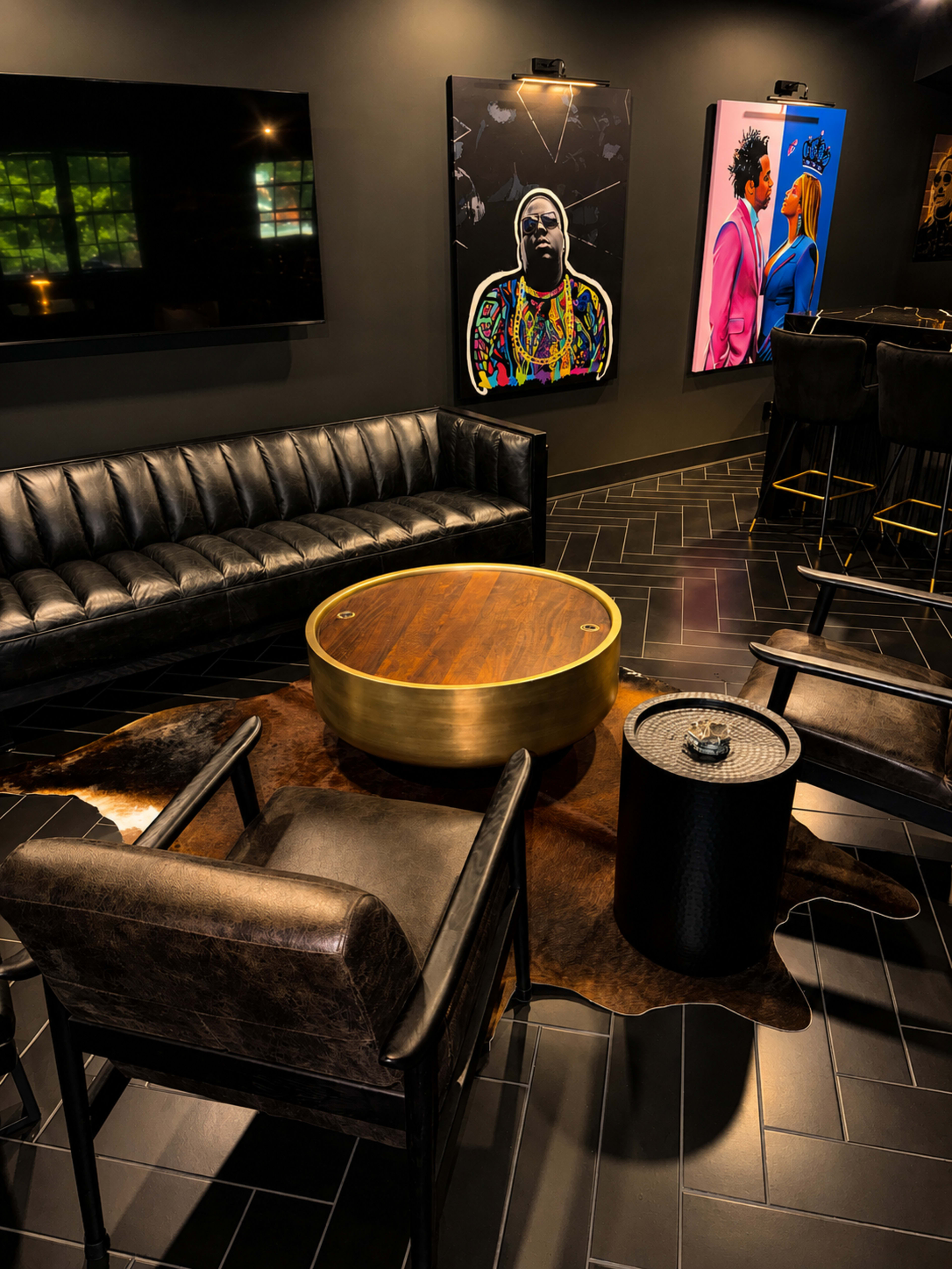 The image shows a stylish lounge area featuring a black leather sofa, two matching chairs, a round wooden coffee table, and art pieces on the wall.