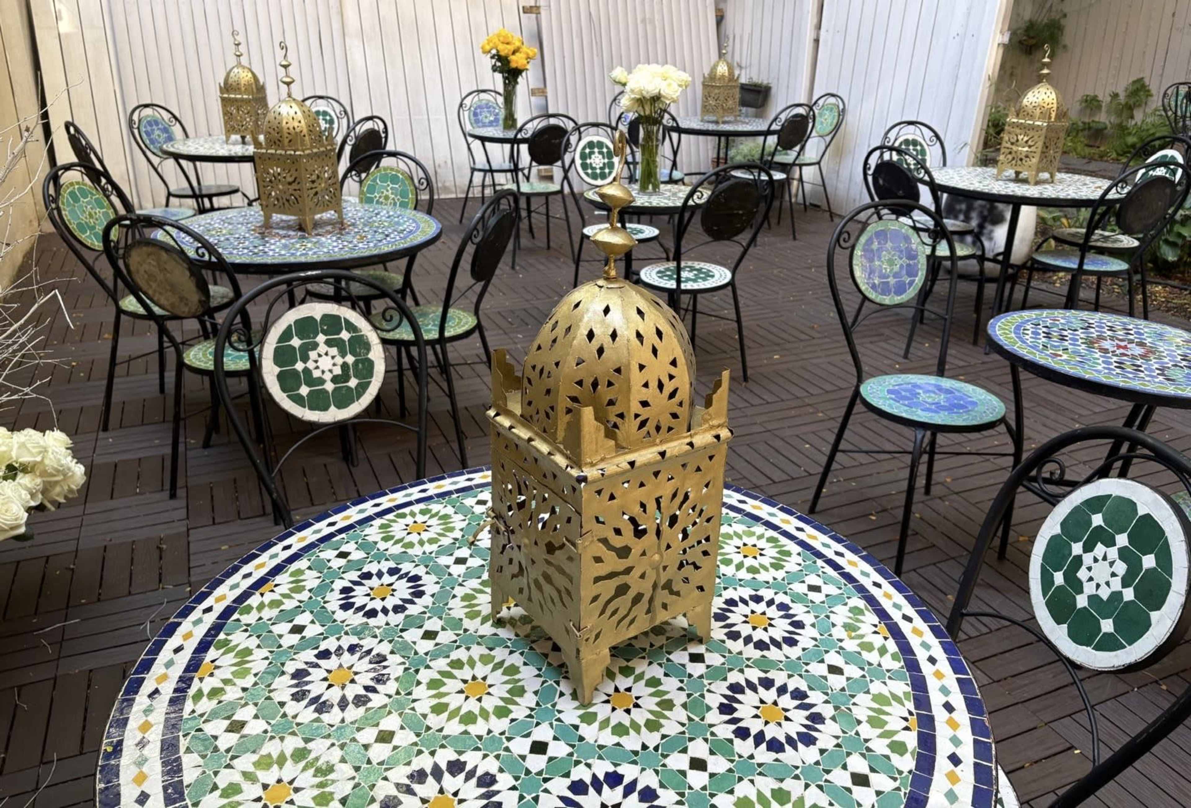 The image features intricately designed Moroccan-style tables and chairs set in an outdoor area, with decorative lanterns placed on the tables.