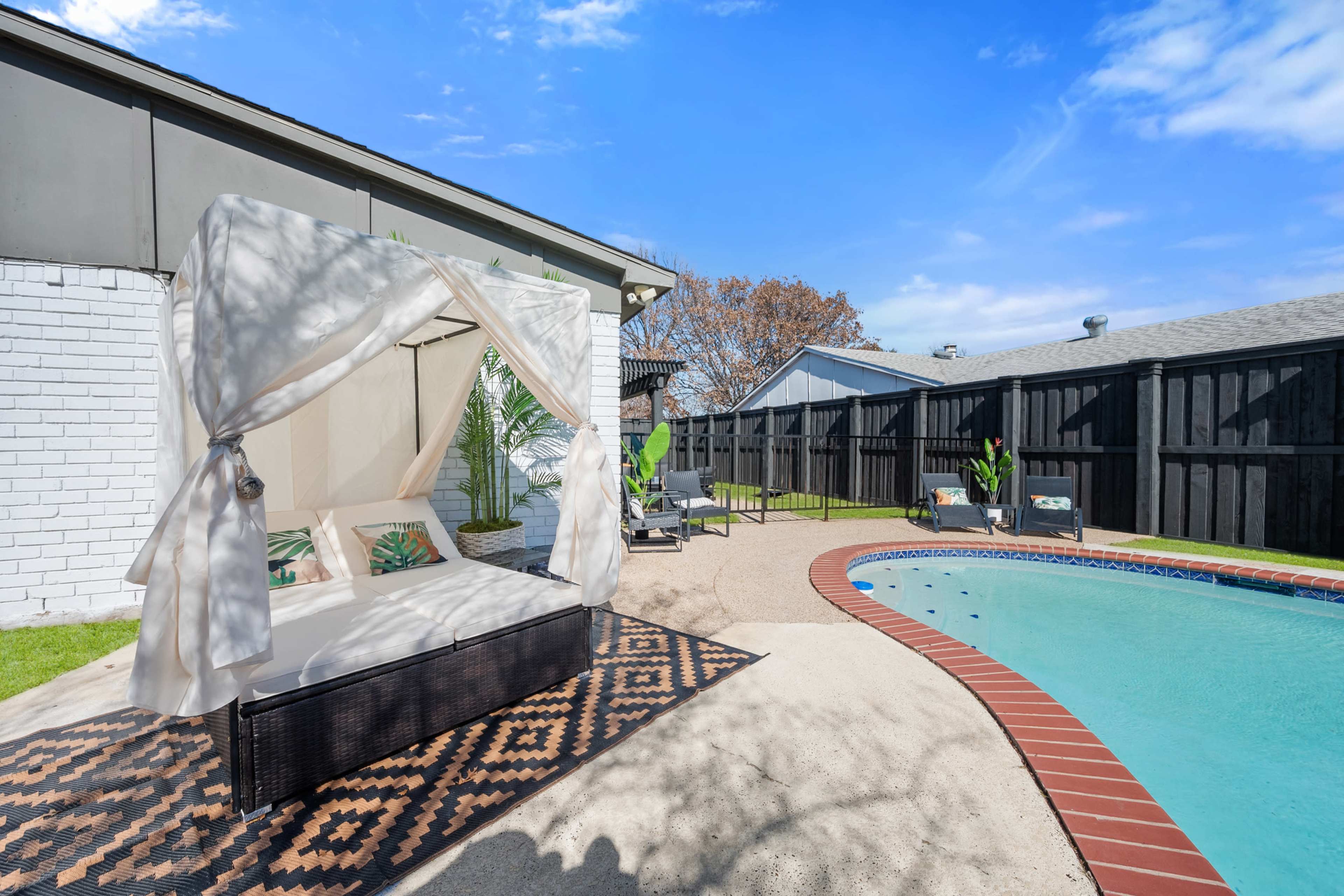 A backyard pool area featuring a covered seating space and a well-maintained swimming pool surrounded by greenery.