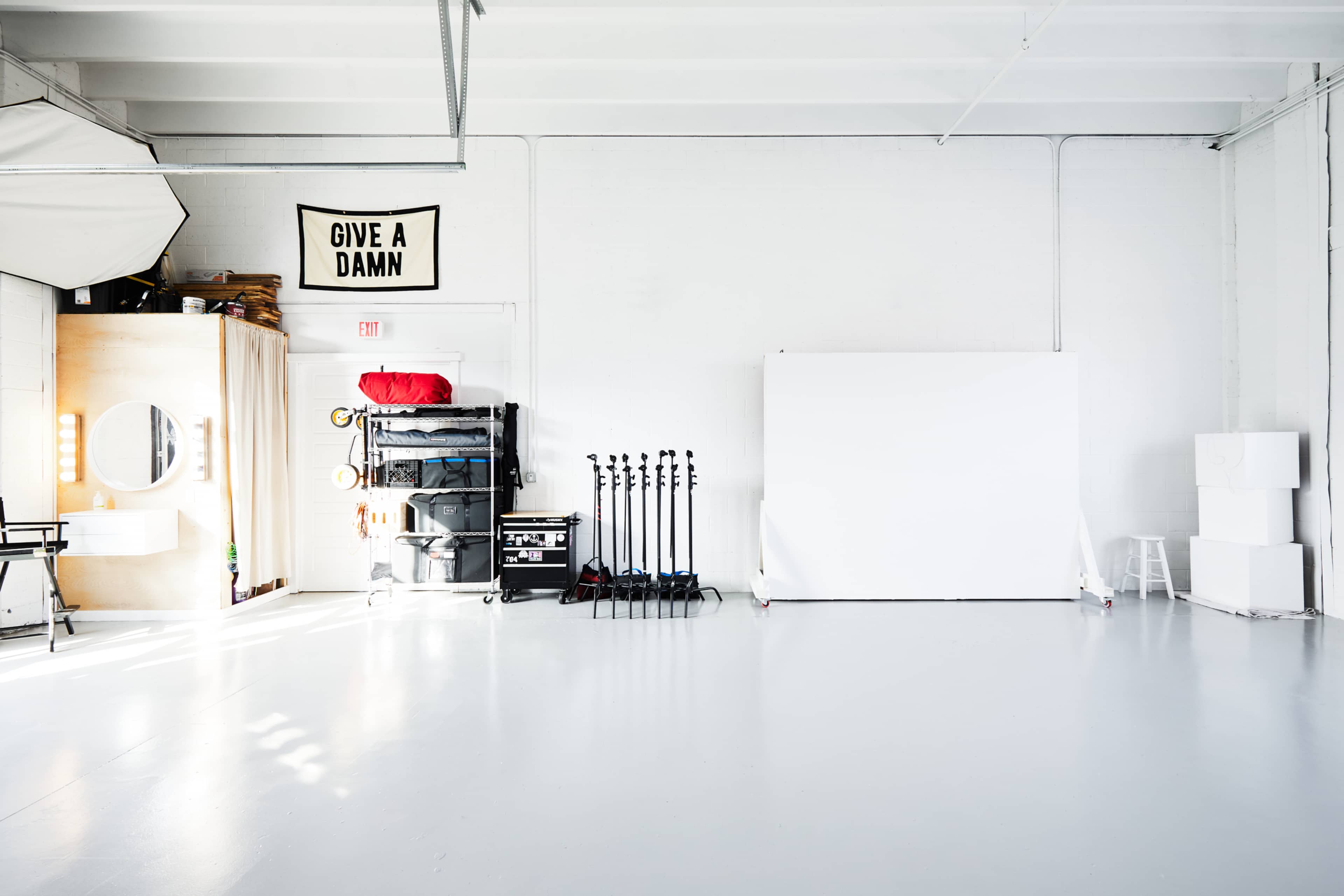 A bright, empty studio space featuring a white backdrop, equipment stands, and a wall sign that reads "GIVE A DAMN."