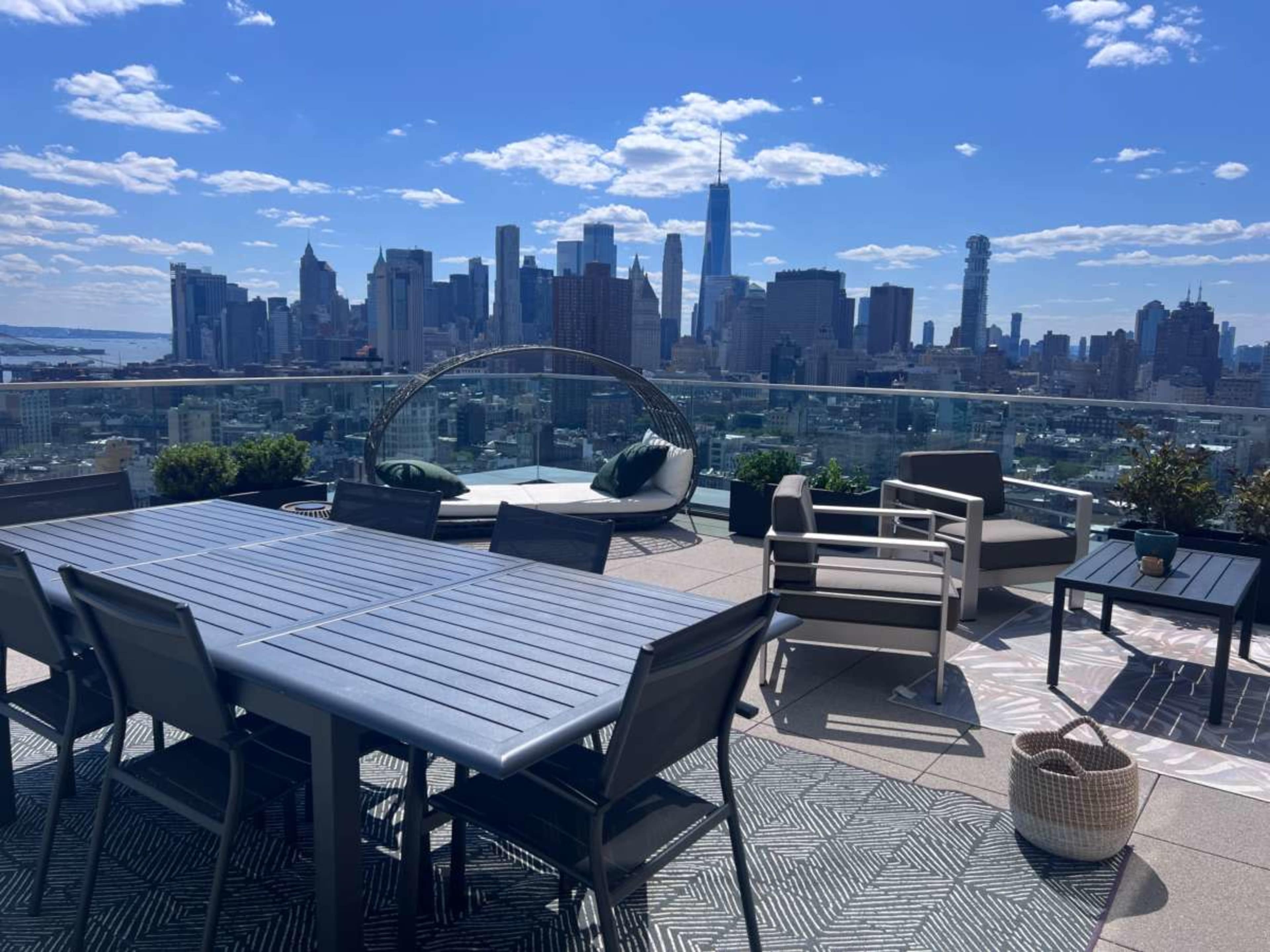 A rooftop terrace features modern outdoor furniture with a view of the New York City skyline.