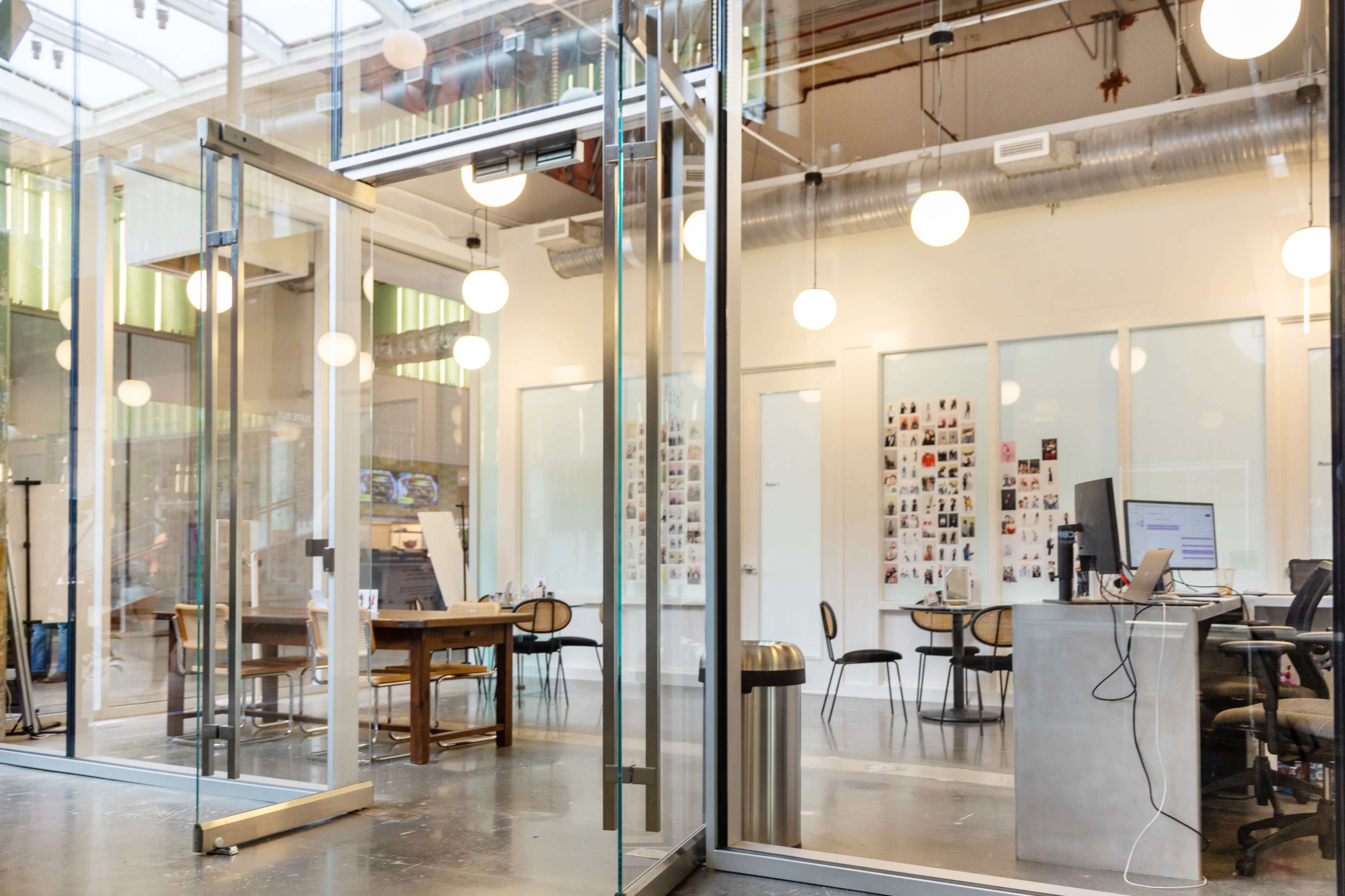 A modern office space features glass walls, a central table, and workstations with computers.