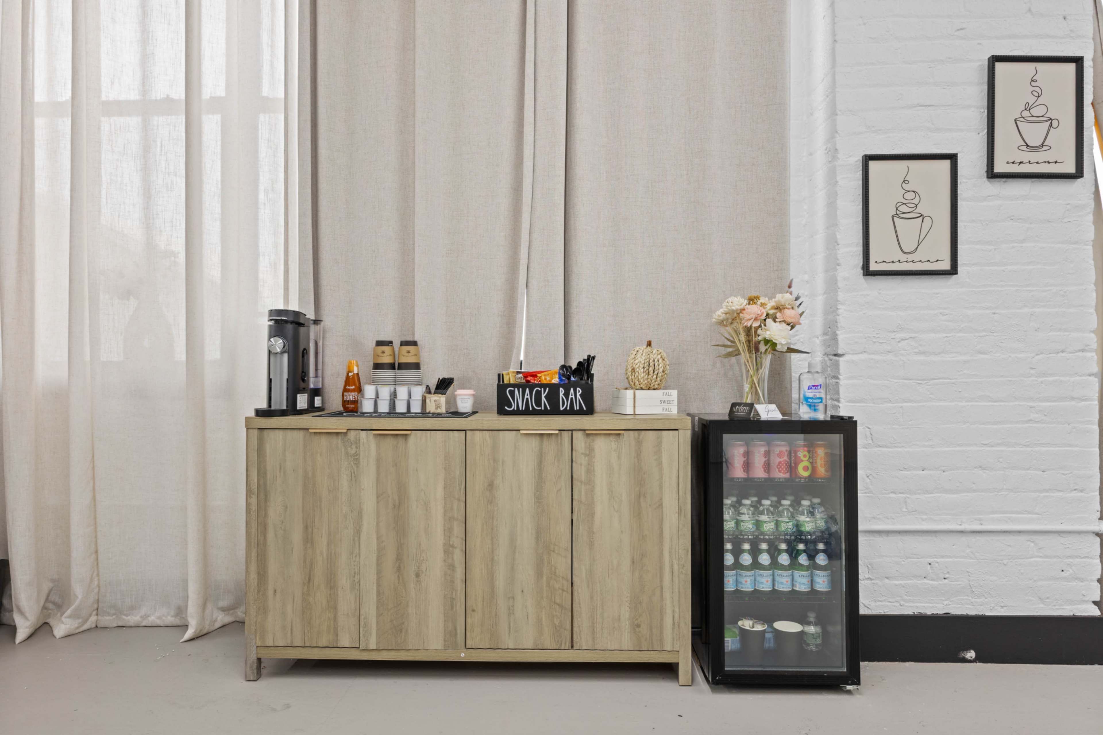 The image features a snack bar with a wooden cabinet displaying beverages, a coffee maker, and decorative items, set against a backdrop of curtains and a white brick wall.