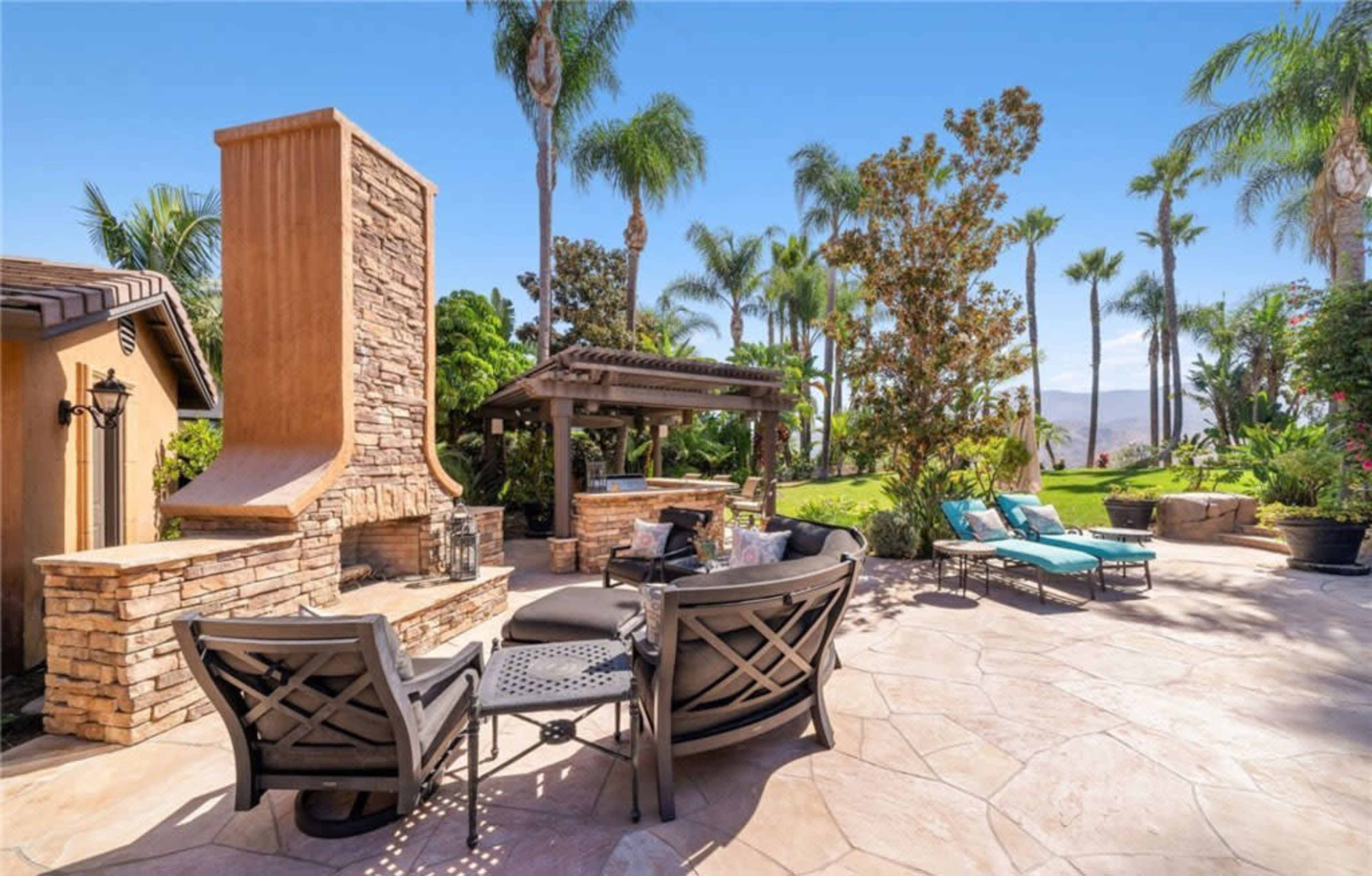 A well-designed outdoor living space featuring a stone fireplace, seating area, and lush greenery.