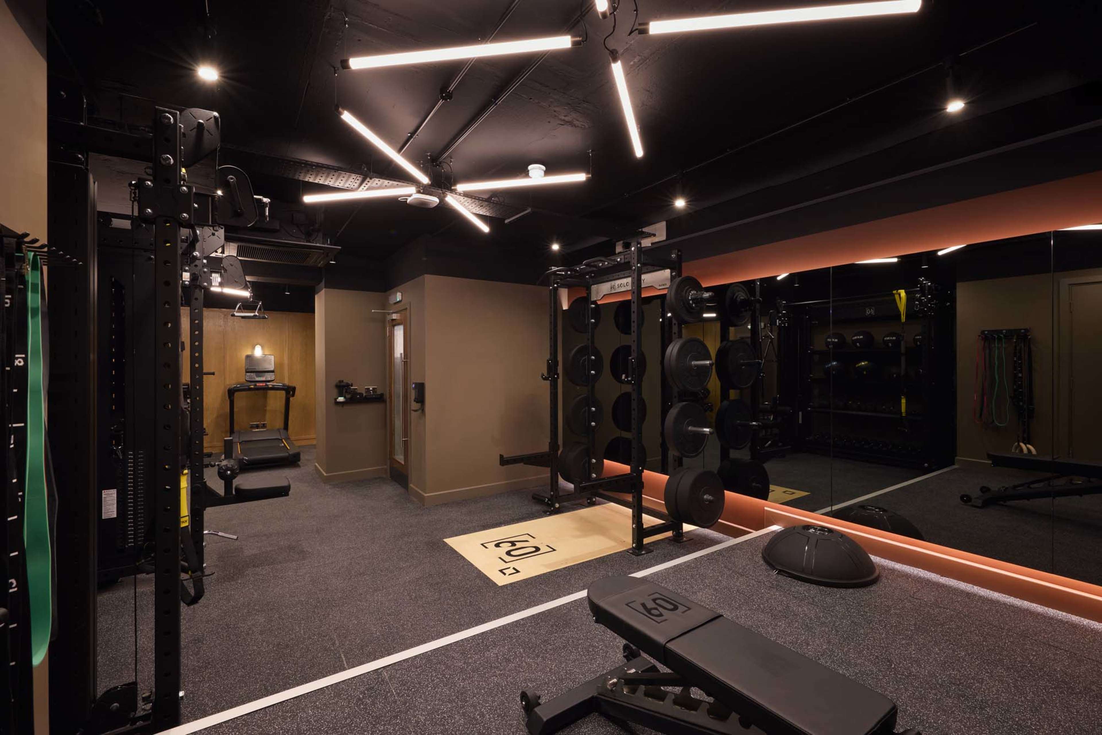 The image shows a modern home gym equipped with various exercise machines, free weights, and a large mirror along one wall.