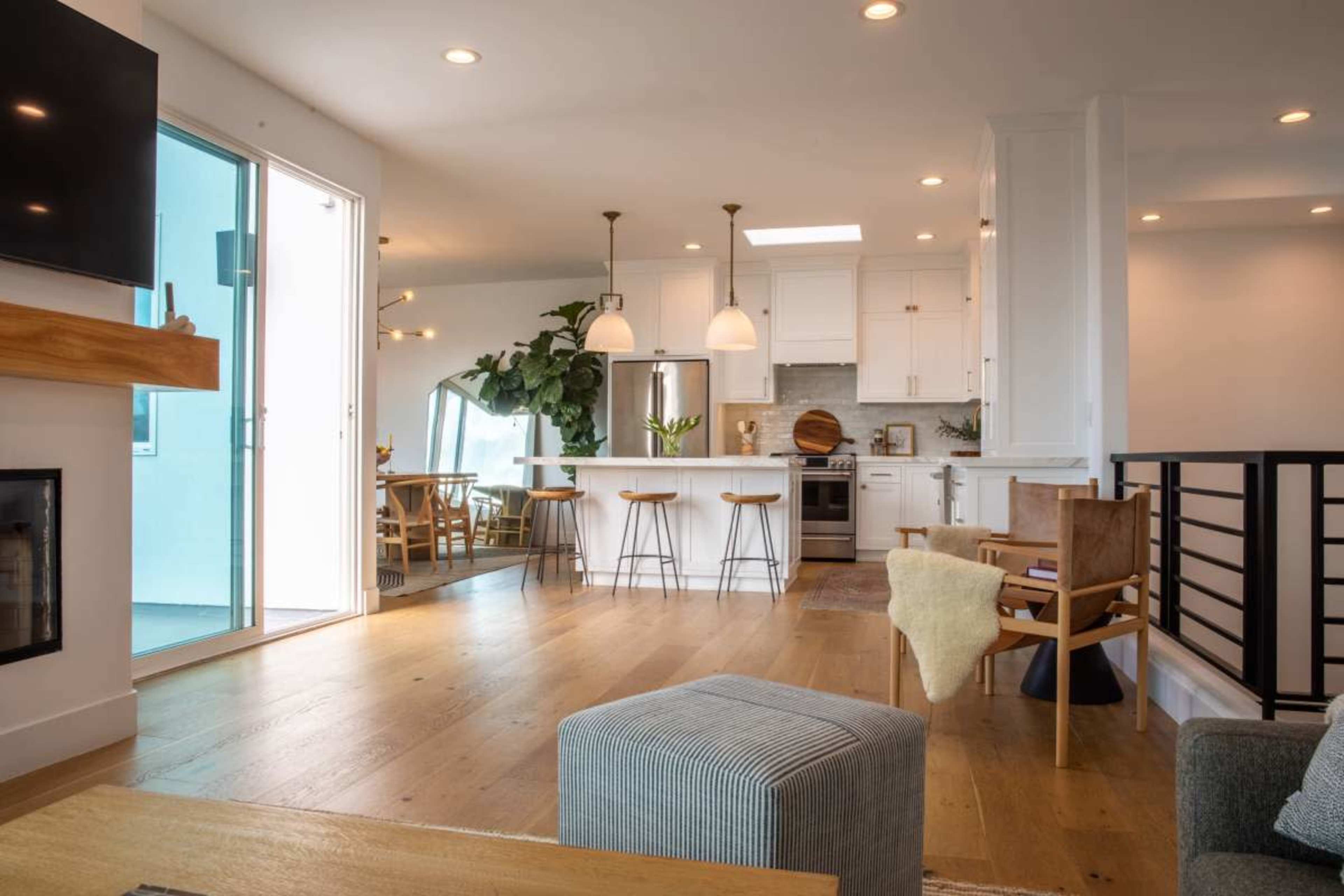 A modern interior living space featuring a kitchen with white cabinets, a dining area, and large windows that provide natural light.