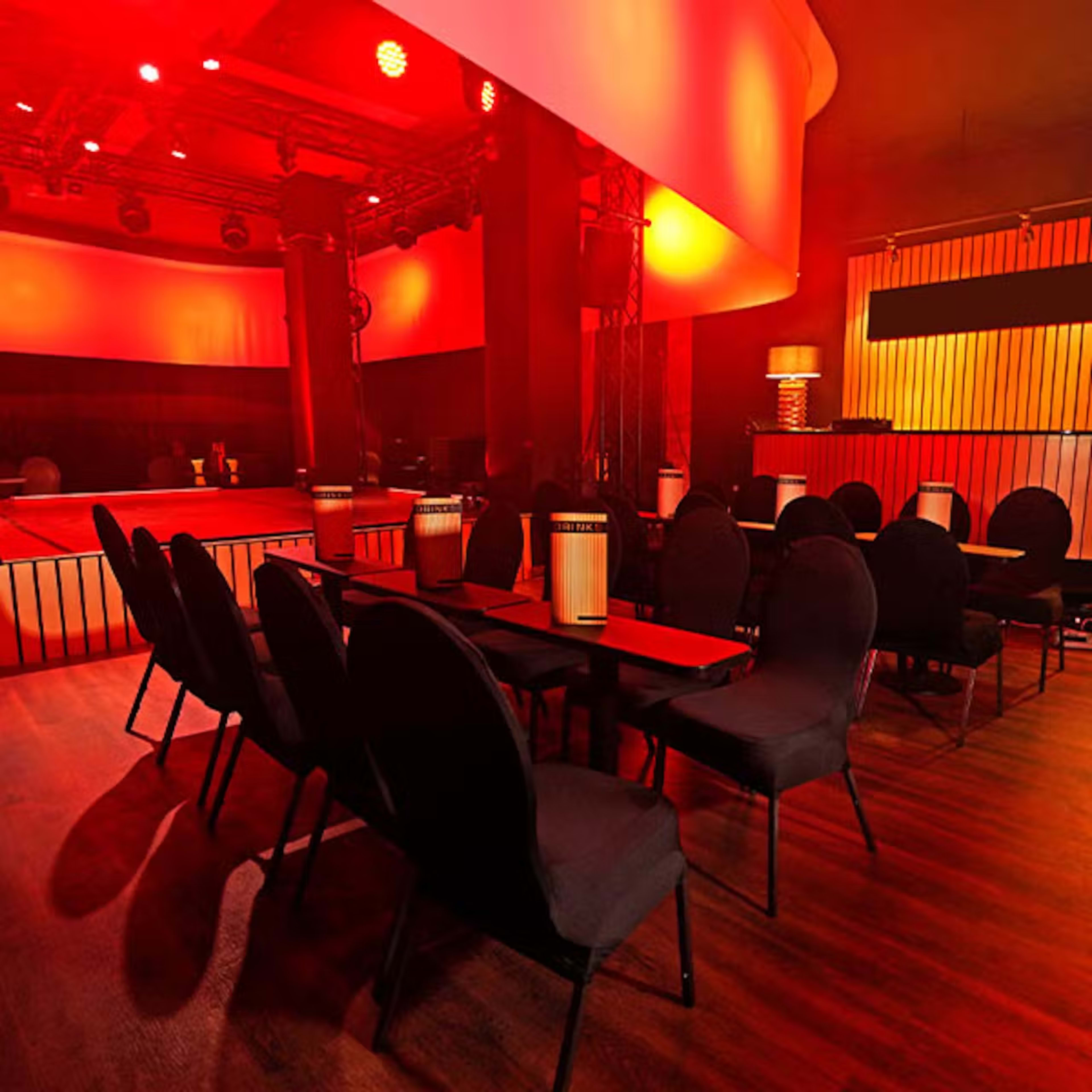 The image shows a dimly lit lounge area with black chairs and tables, illuminated by red lighting.