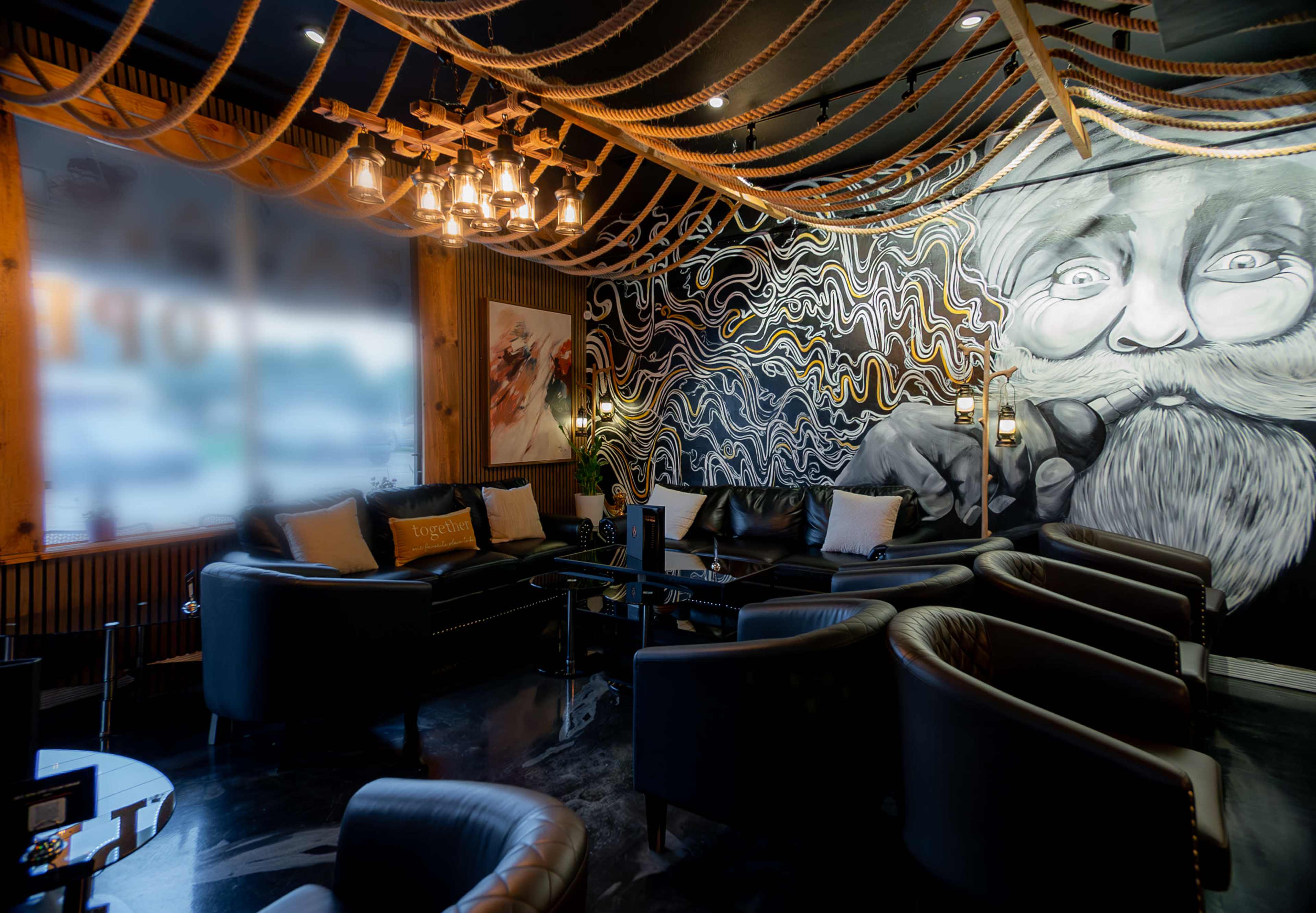 A lounge area with leather seating, a mural of a bearded man on the wall, and decorative rope lighting.