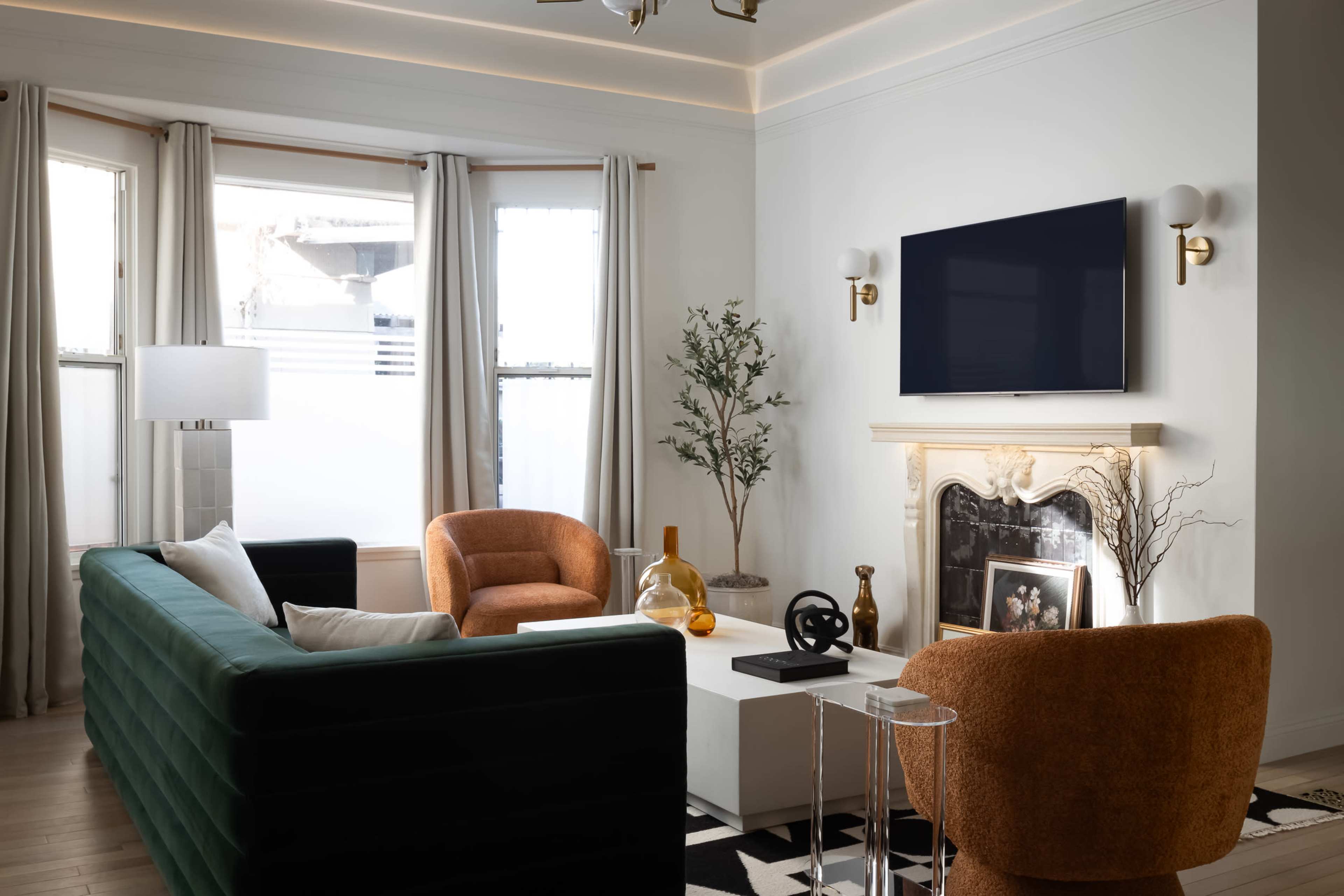 The image shows a modern living room with a green sofa, two armchairs, a coffee table, and a TV mounted above a fireplace.