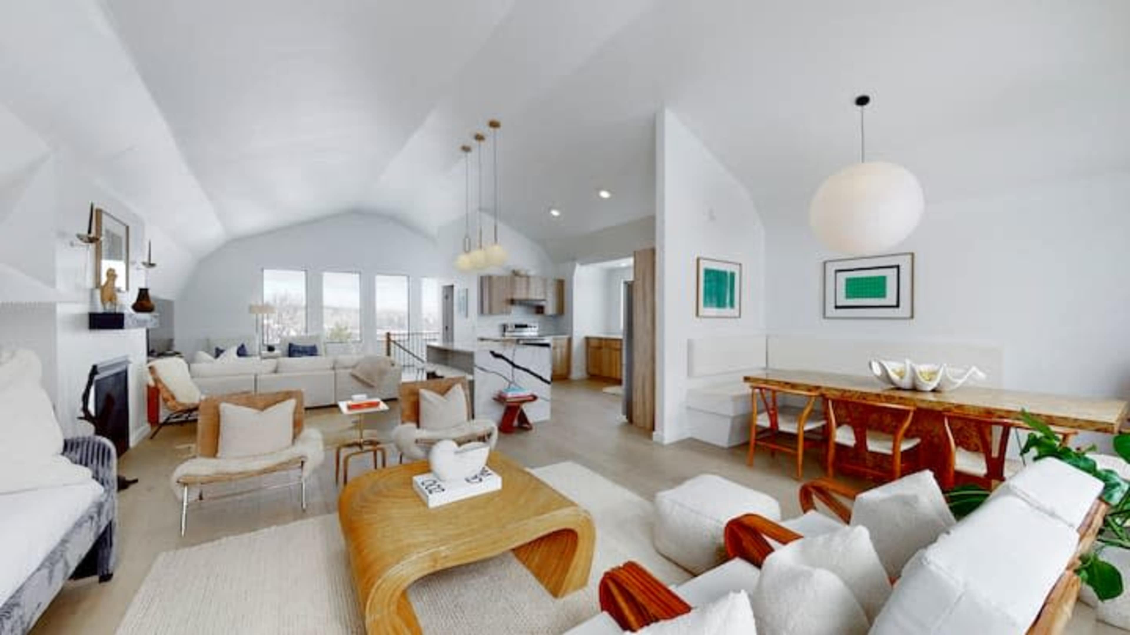 A modern, open-concept living area featuring a seating arrangement, dining table, and kitchen space, all with large windows allowing natural light.