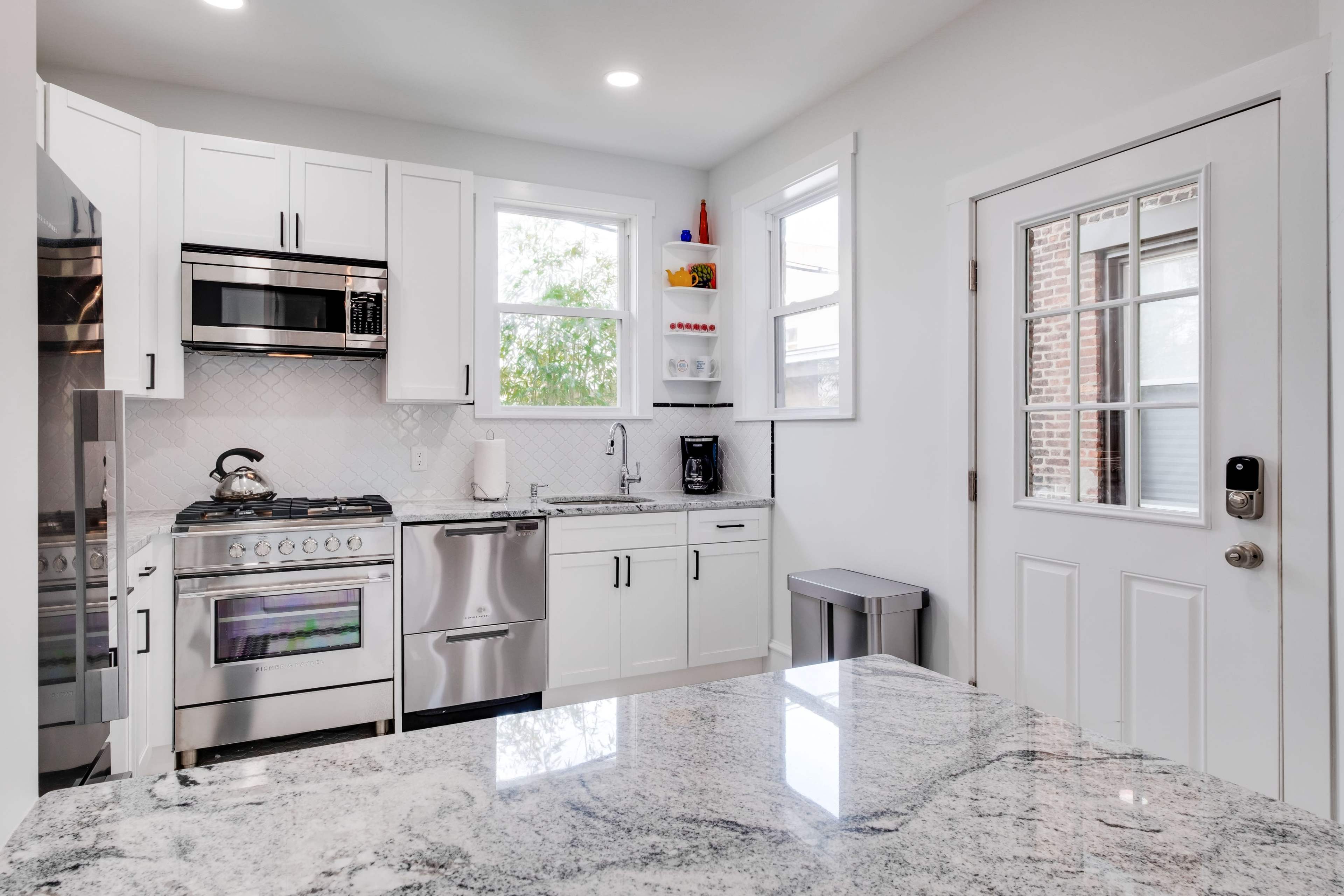 A modern kitchen features stainless steel appliances, white cabinetry, and a granite countertop, with a door leading to the outdoors.