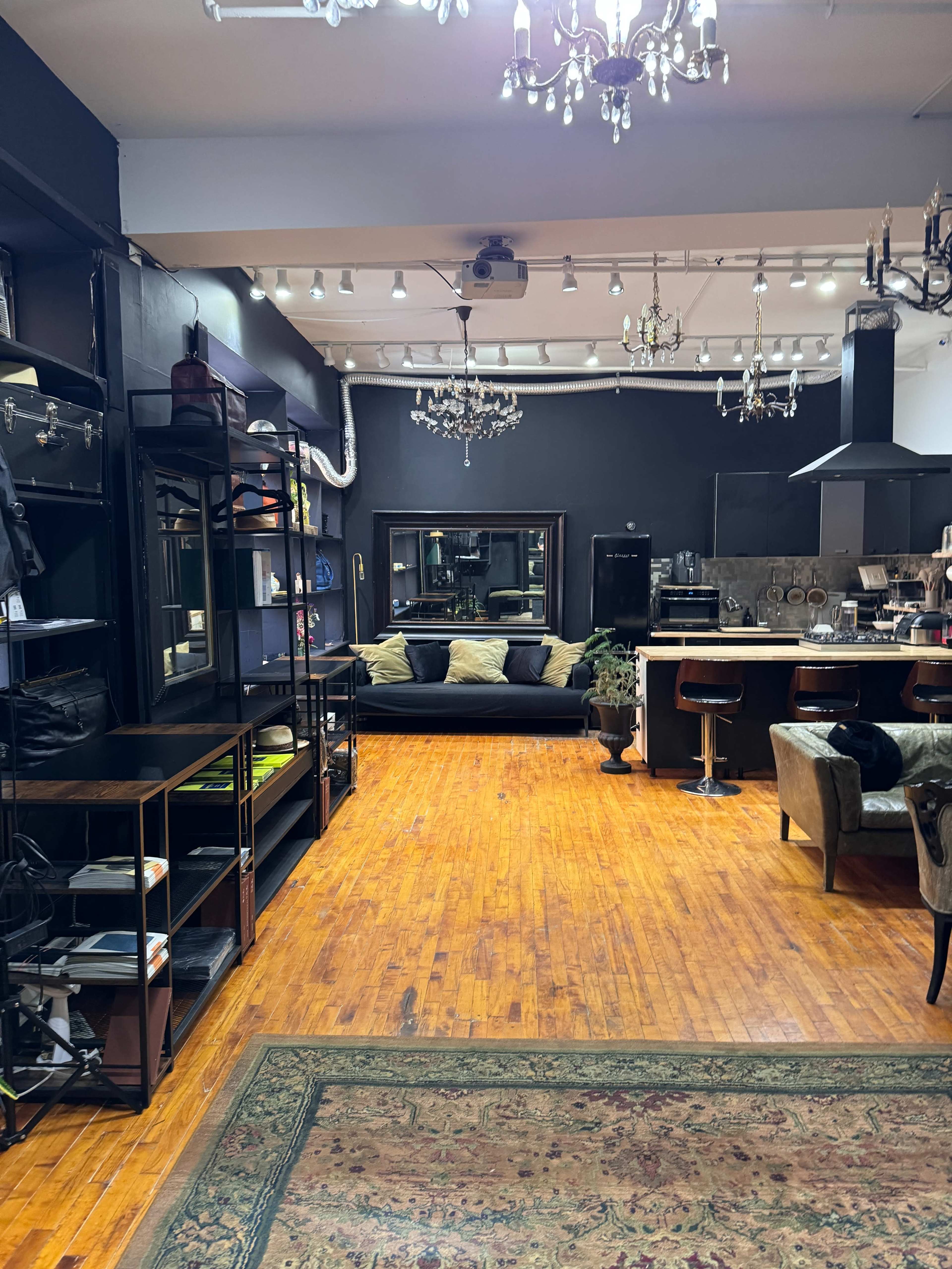 A modern interior space featuring a living area with a dark sofa, shelves, and a kitchen area with bar stools.