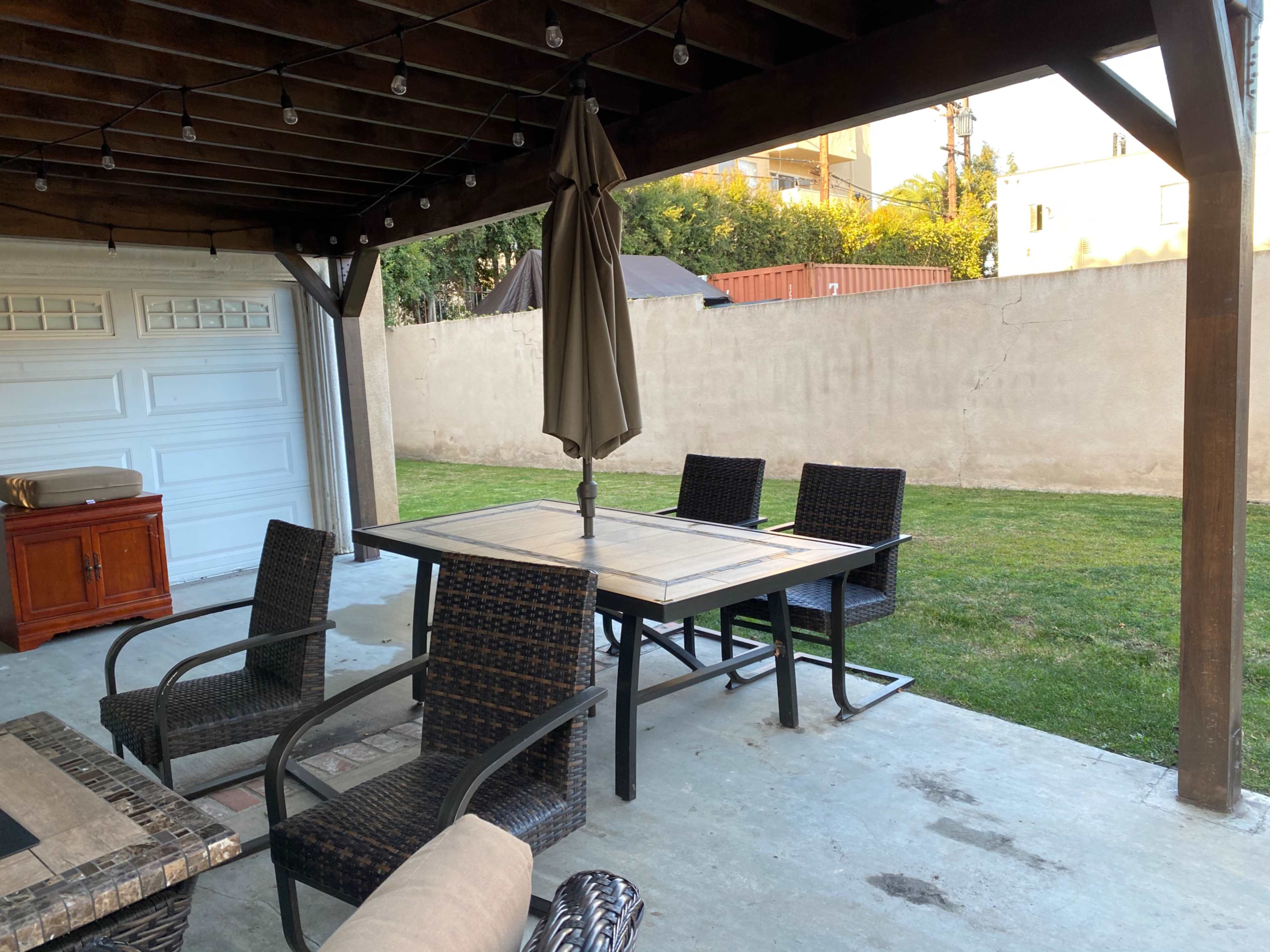 The image shows a covered patio area with a table and four chairs, an umbrella, and a grassy backyard.