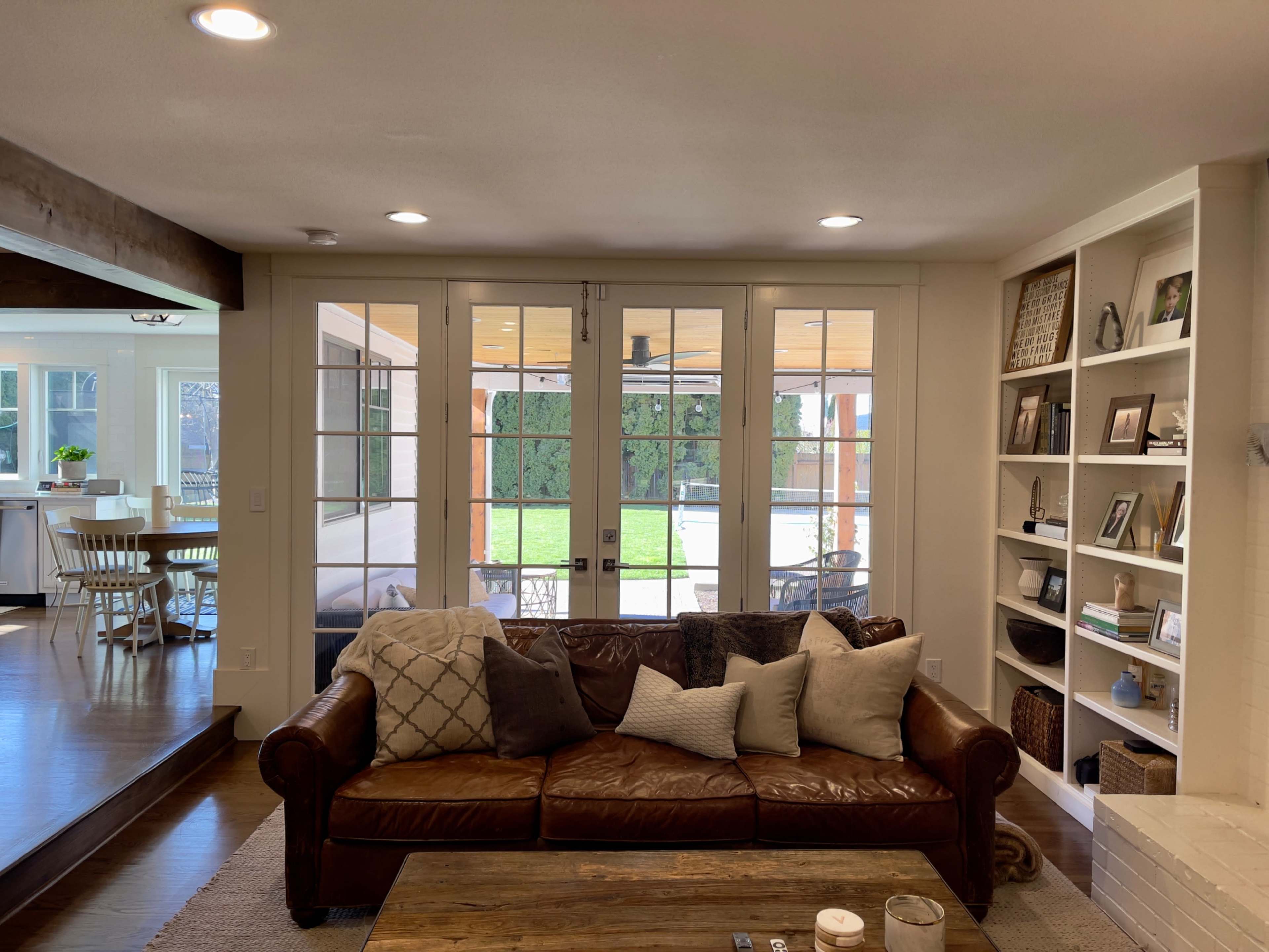 A leather sofa with various throw pillows faces a set of French doors that open to a patio and backyard area.