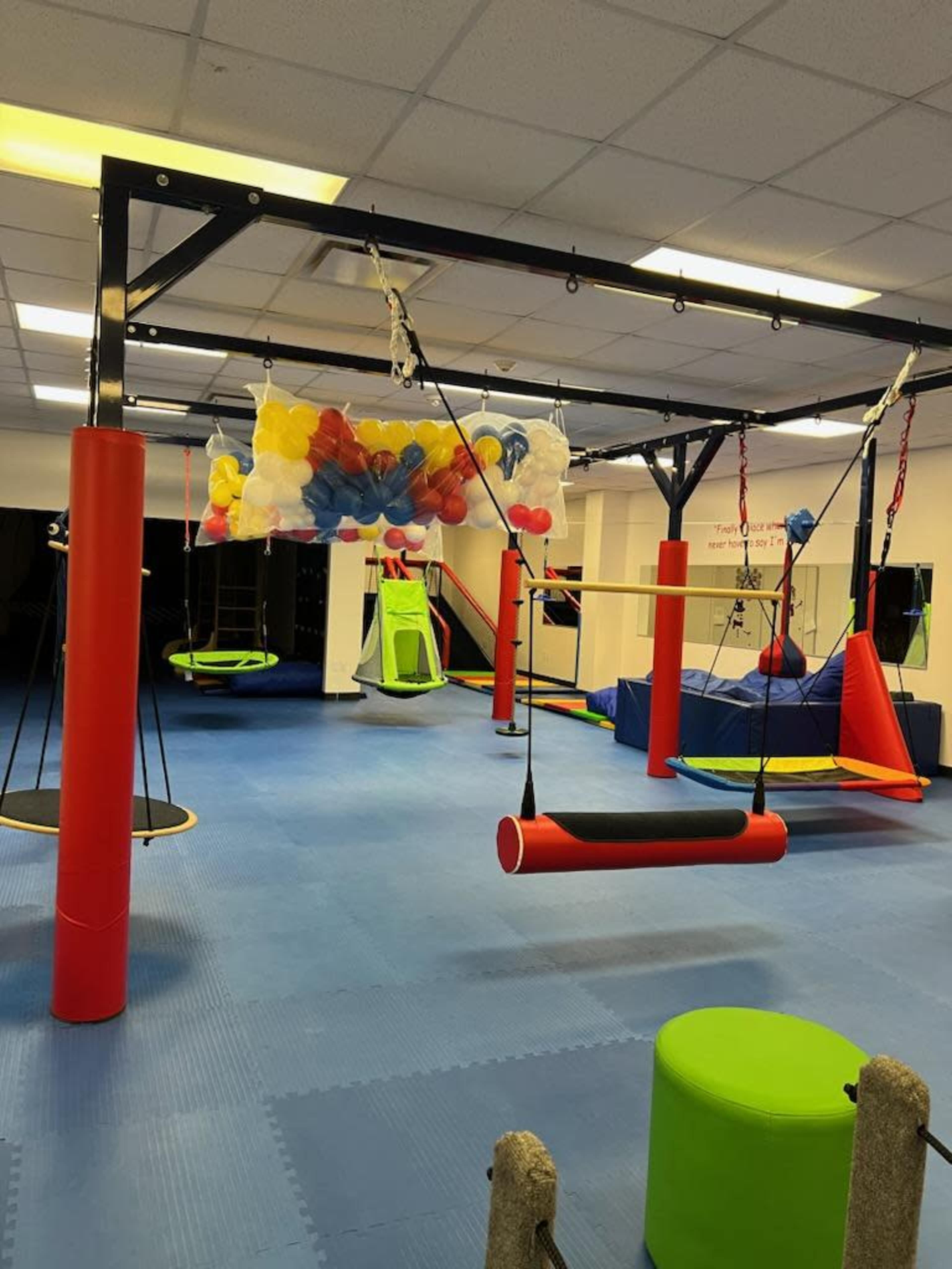 An indoor play area equipped with various colorful equipment, including swings and climbing structures, set against a rubber mat flooring.