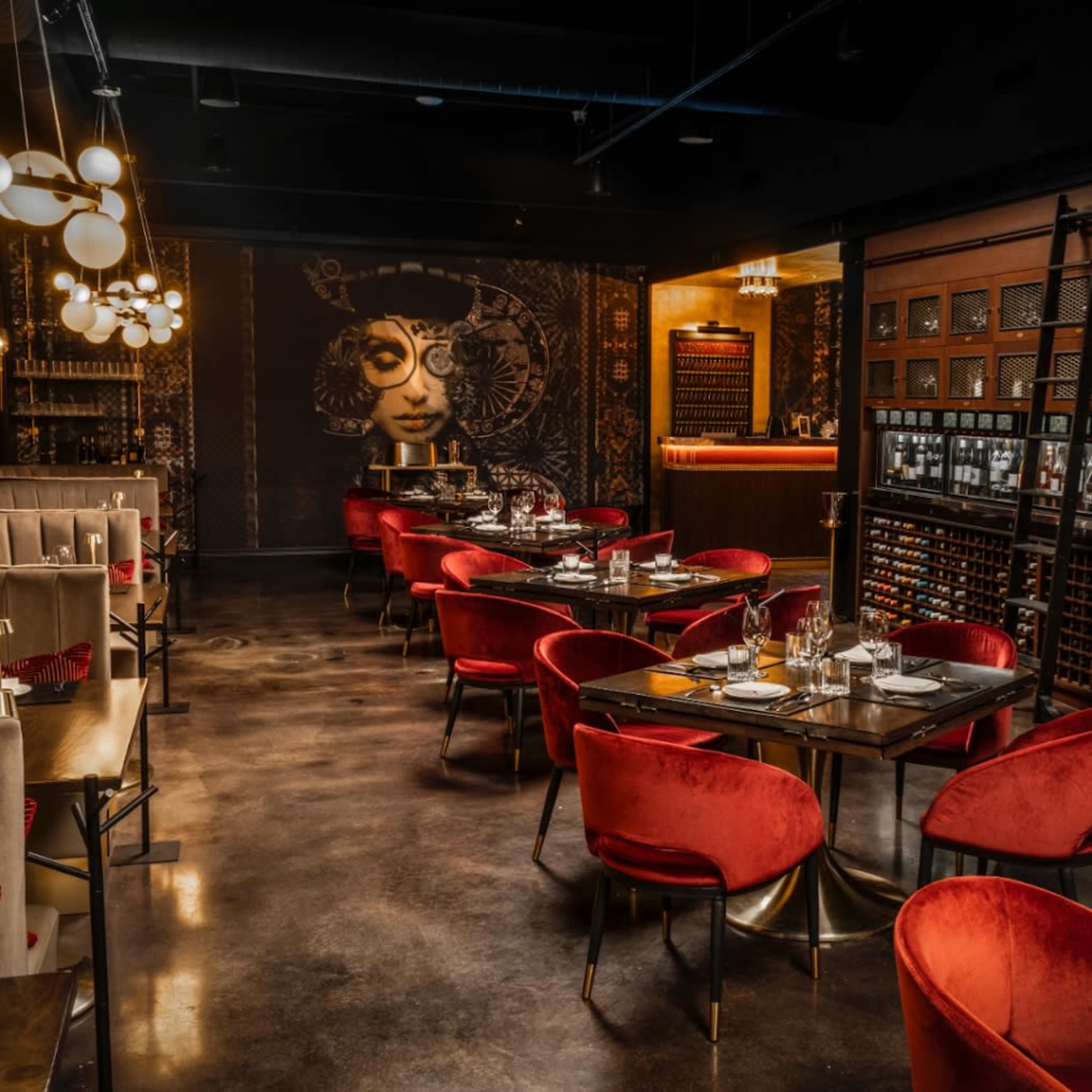 The restaurant features plush red chairs and dark wood tables arranged in a stylish dining area, accented by contemporary lighting and artwork on the walls.