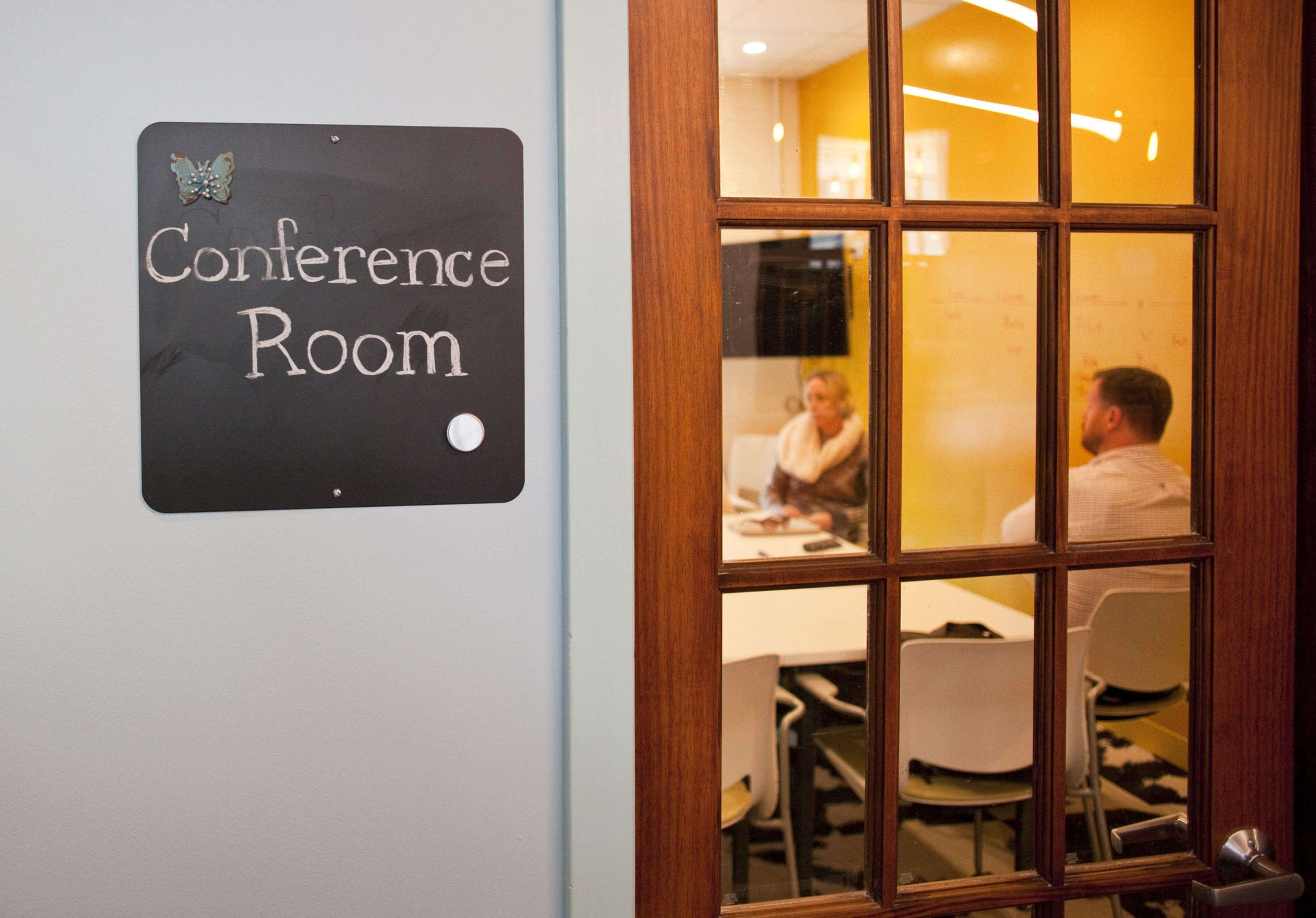 A door with a sign reading "Conference Room" opens into a meeting space where two people are seated at a table.