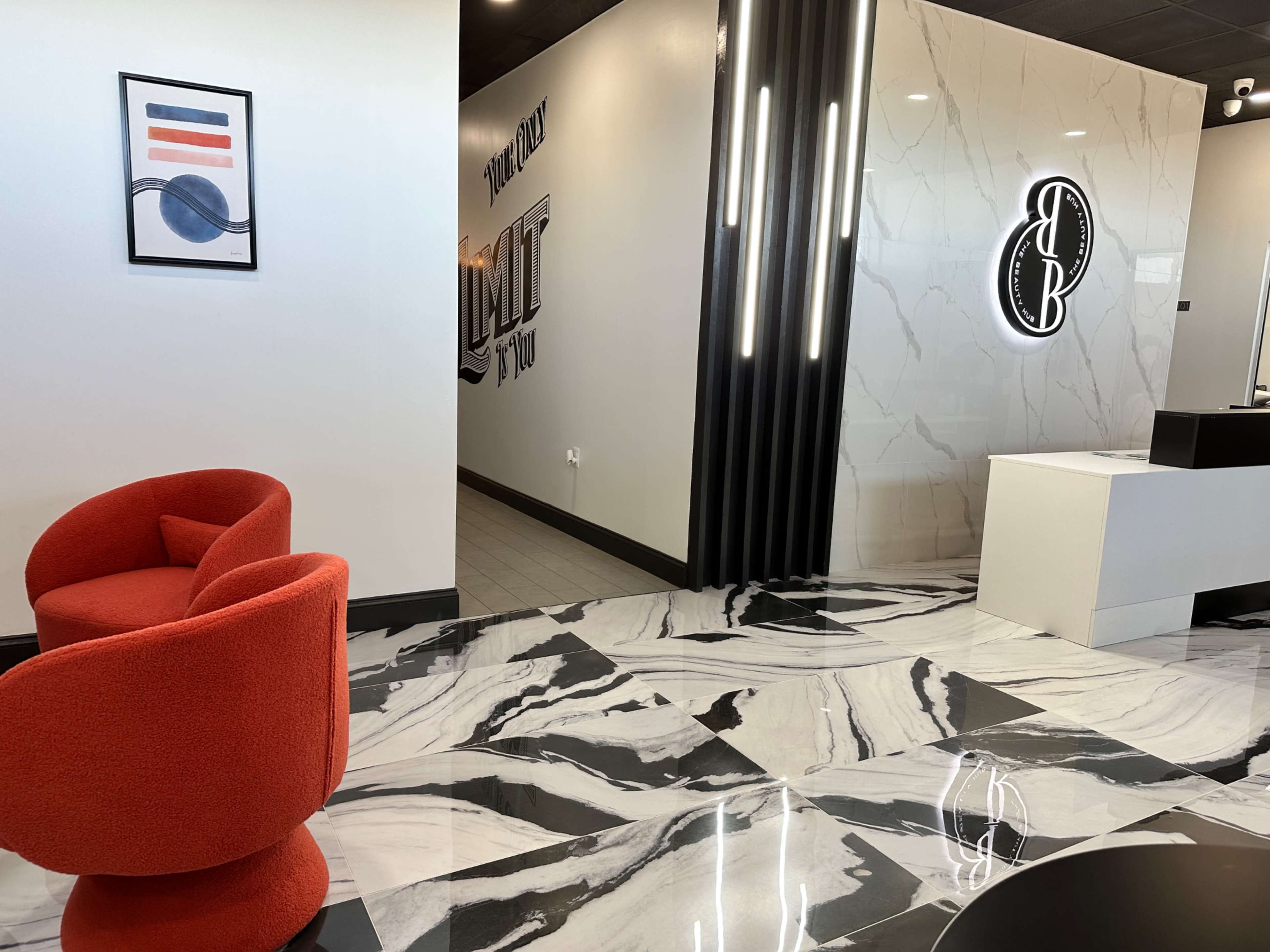 A modern interior design featuring a reception area with a red chair, a marble floor, and a decorative wall with illuminated signage.