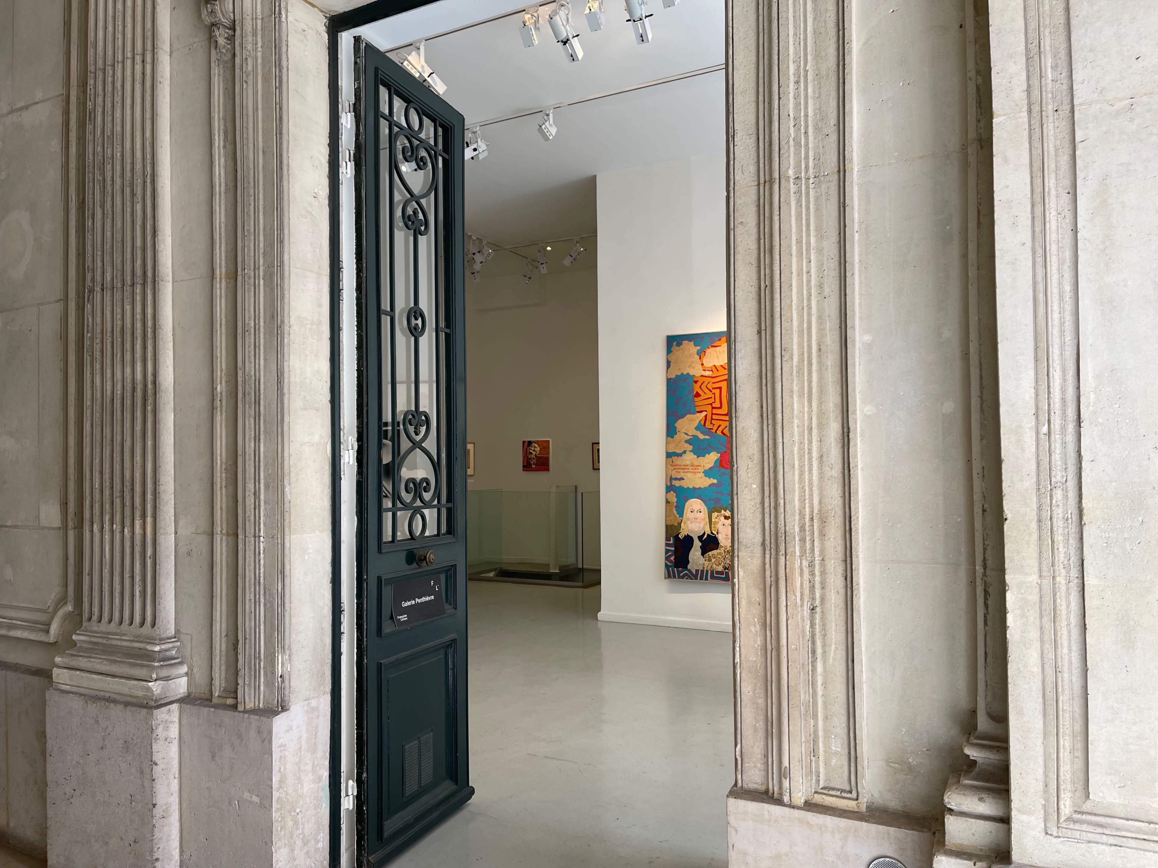 A large black door stands open, revealing a spacious art gallery with colorful artworks displayed on the walls.