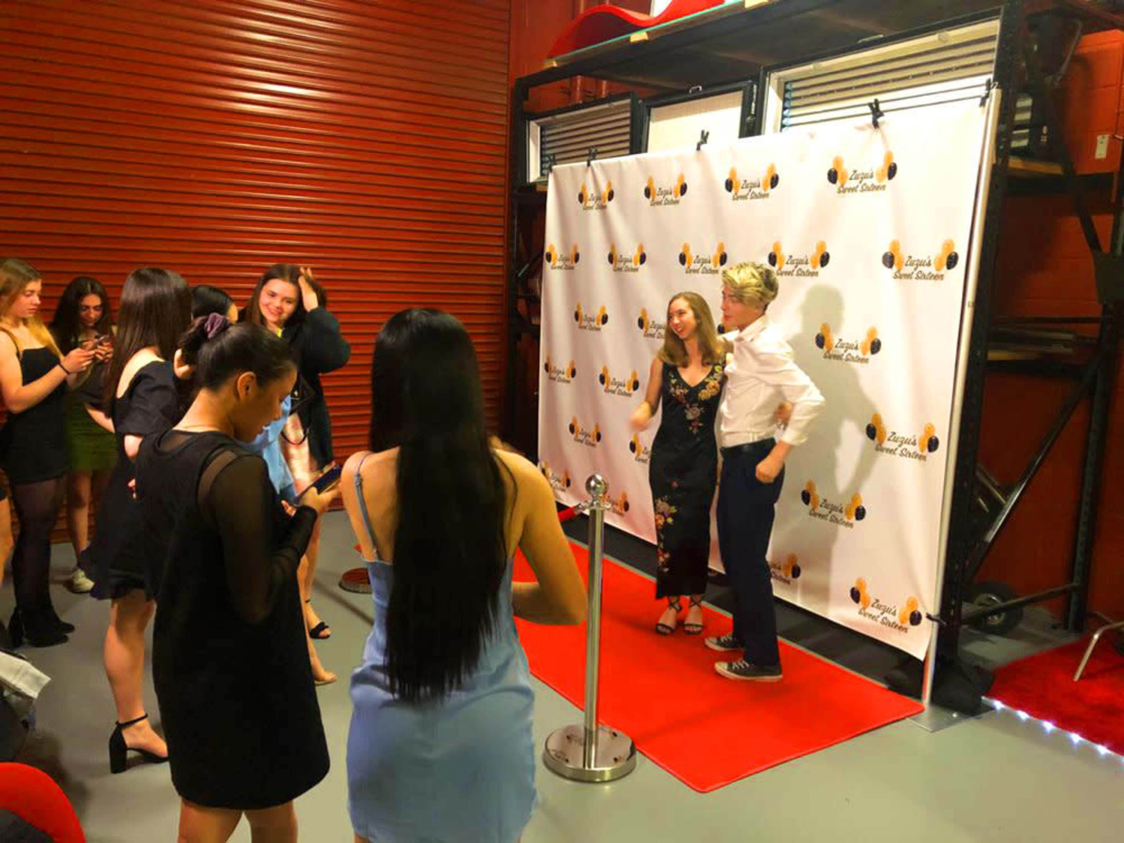 A group of people gather by a red carpet backdrop for a photo opportunity at an event.