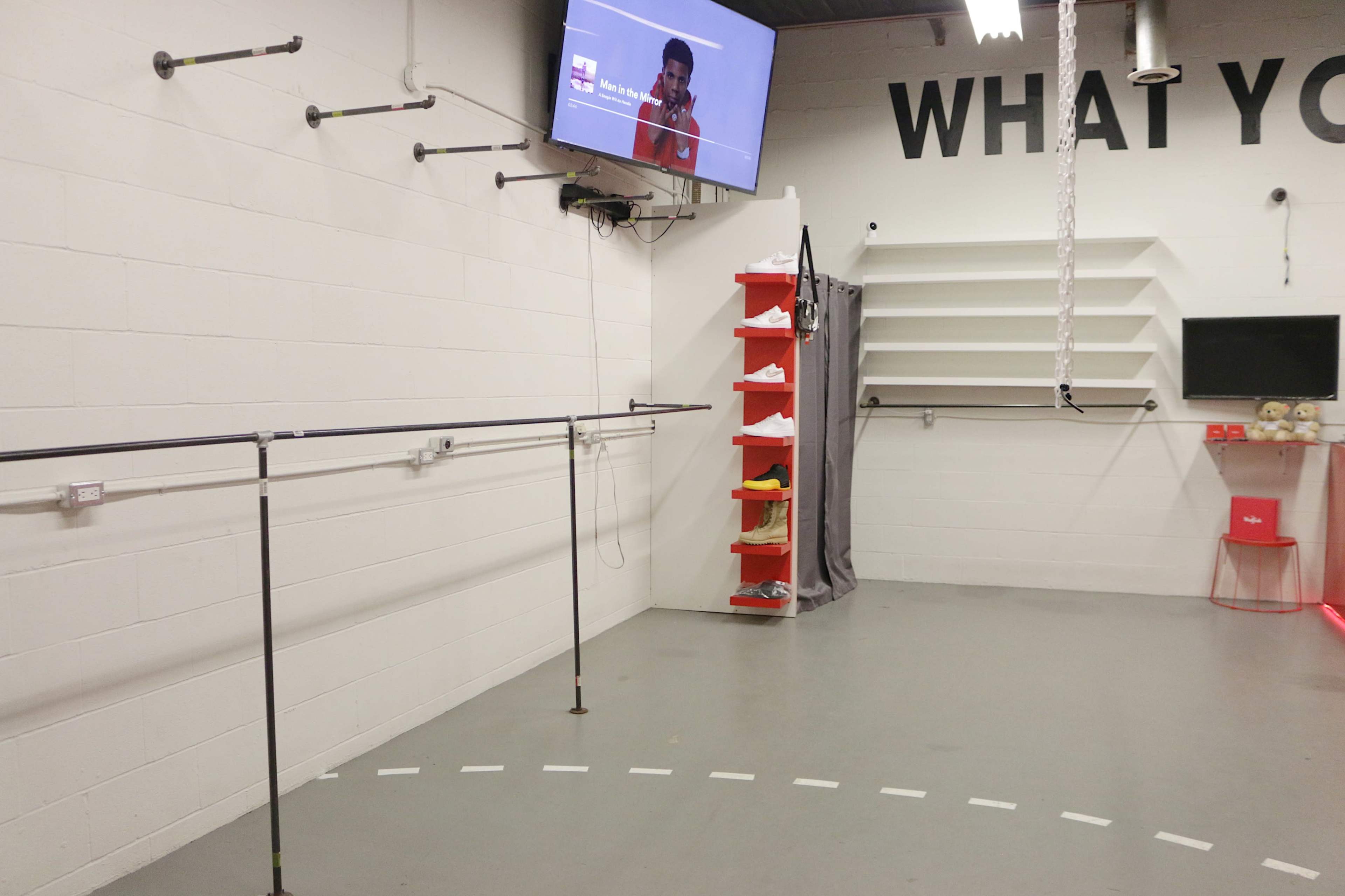 A sparse indoor space with wall-mounted bars, shelves, and a screen displaying a video, along with a series of shoe storage units.