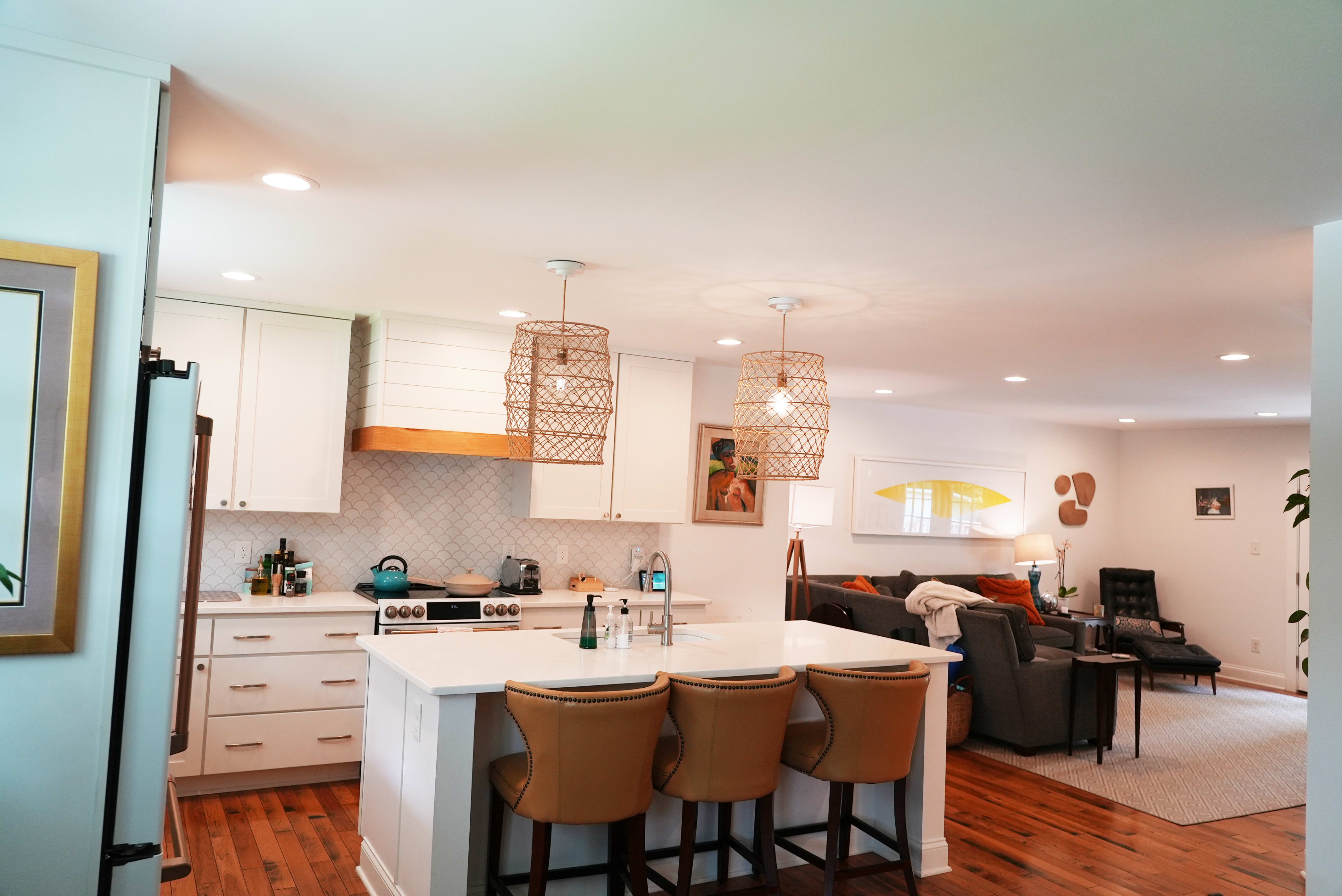 A modern kitchen with white cabinets, a large island with seating, and a living area in the background featuring a sofa and armchairs.