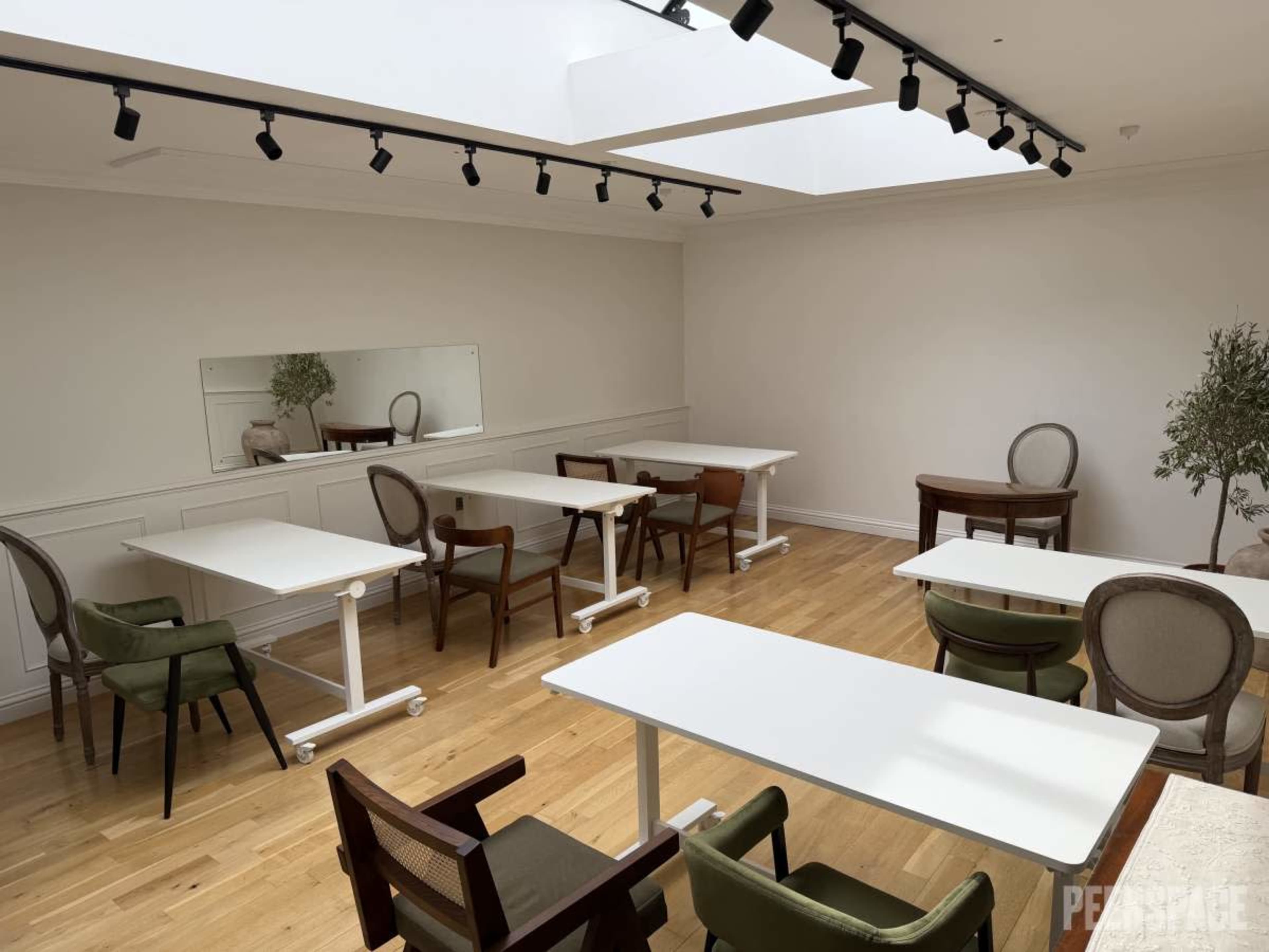 The room features several tables and chairs arranged in a bright, minimalist space with a skylight and a mirror on one wall.