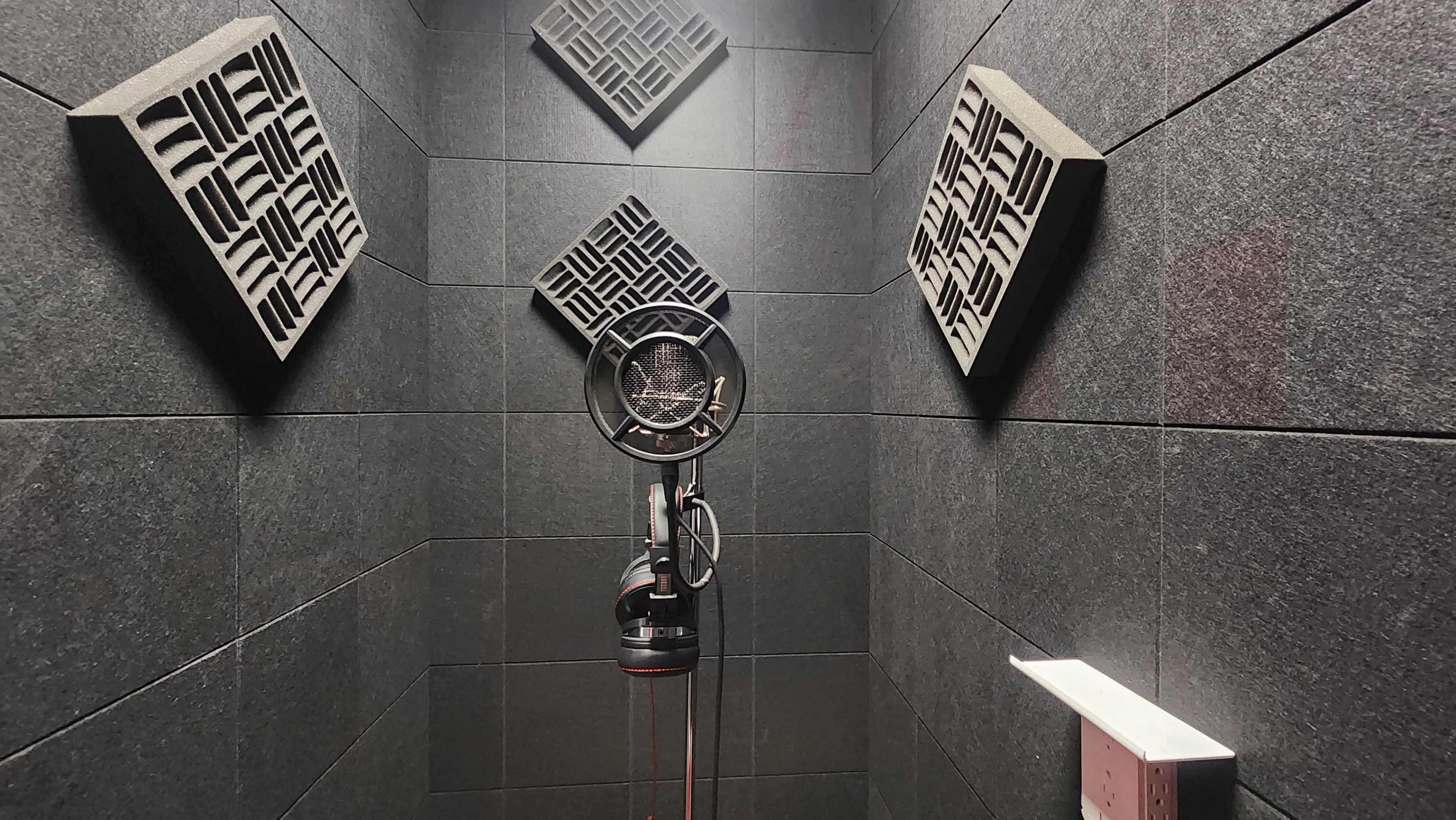 A soundproof vocal booth with acoustic panels on the walls and a microphone on a stand in the center.