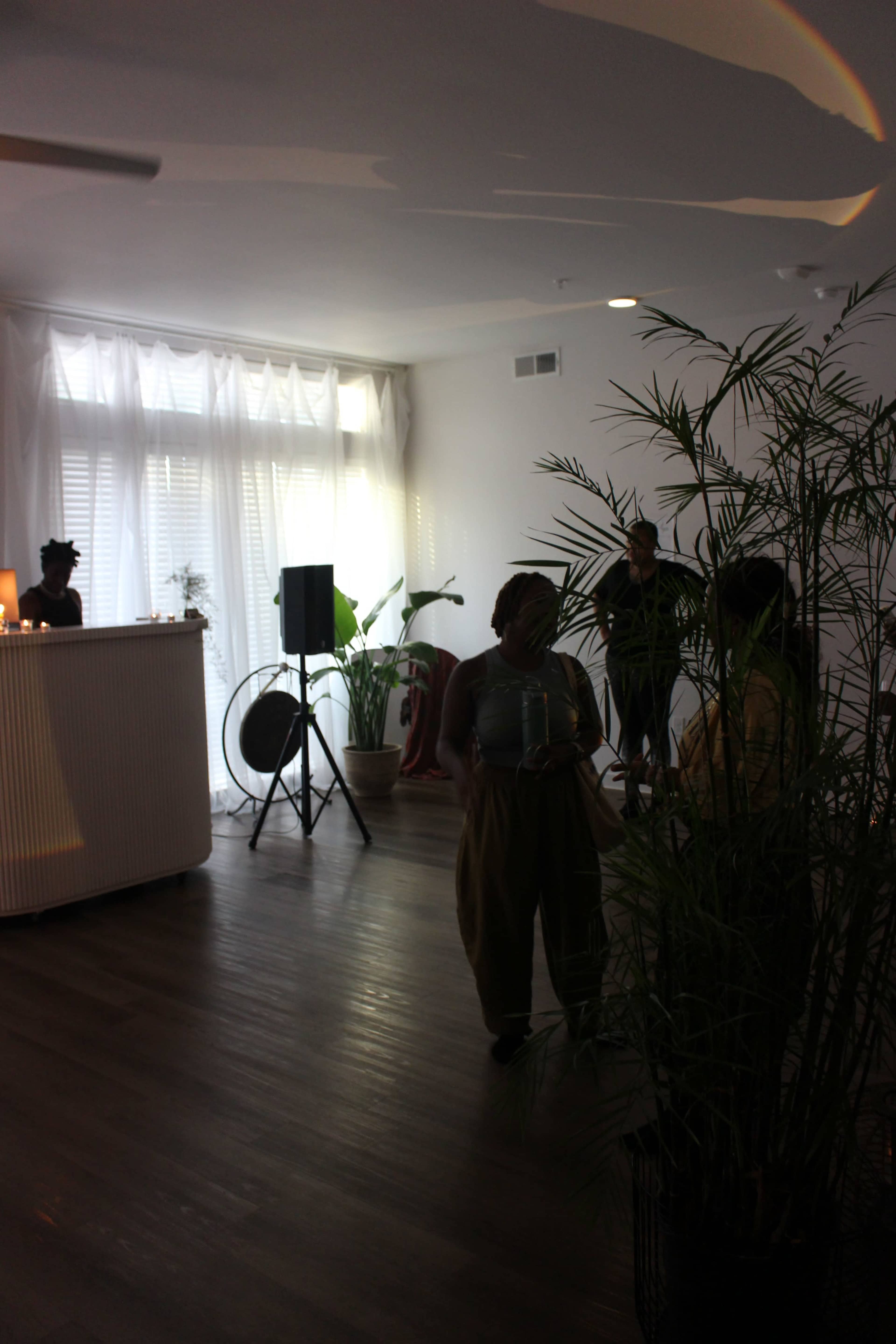 The image shows a modern, well-lit interior space with plants, a bar area, and people engaged in conversation.