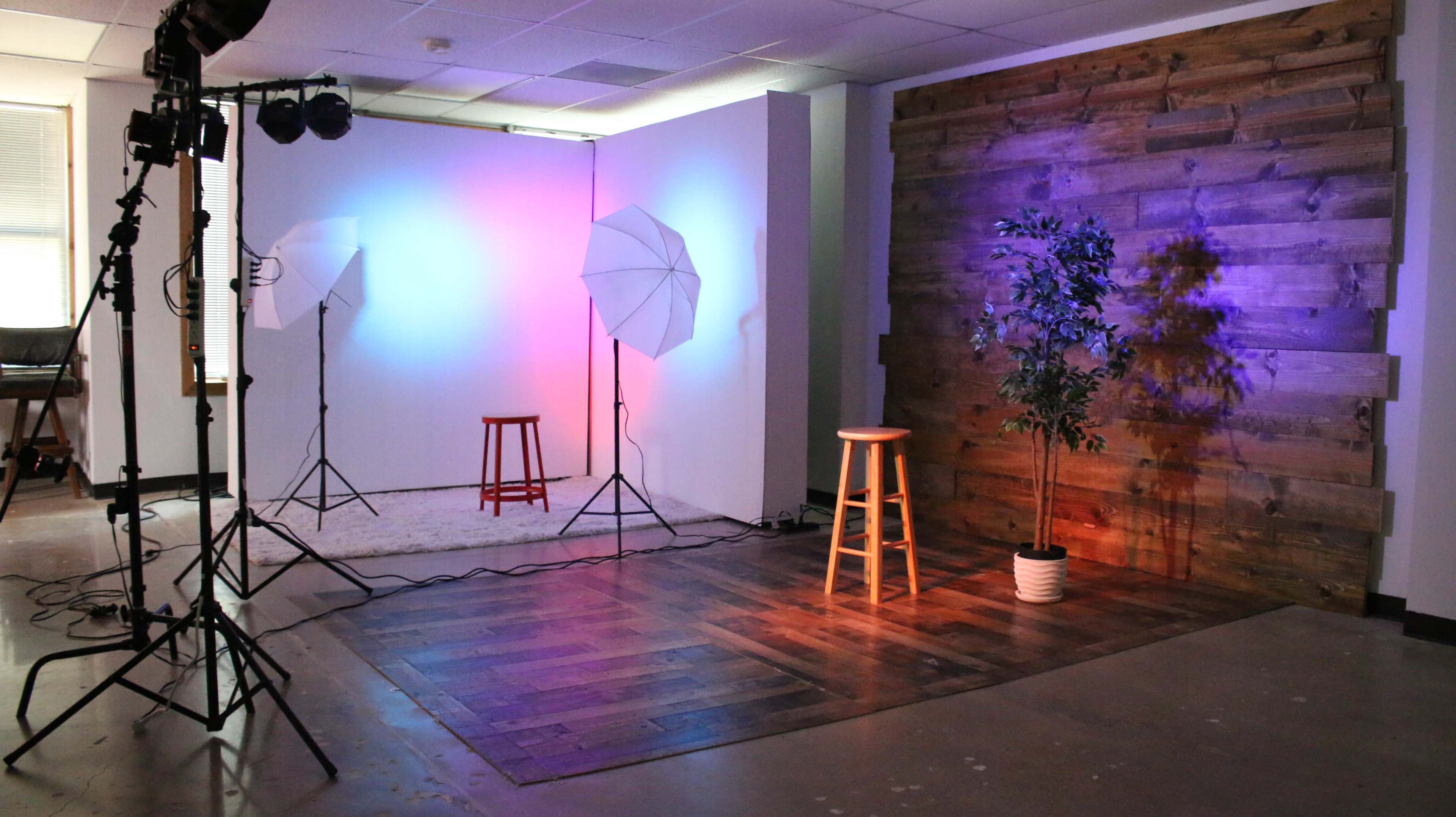A photography studio with softbox lights, two wooden stools, and a wooden accent wall.