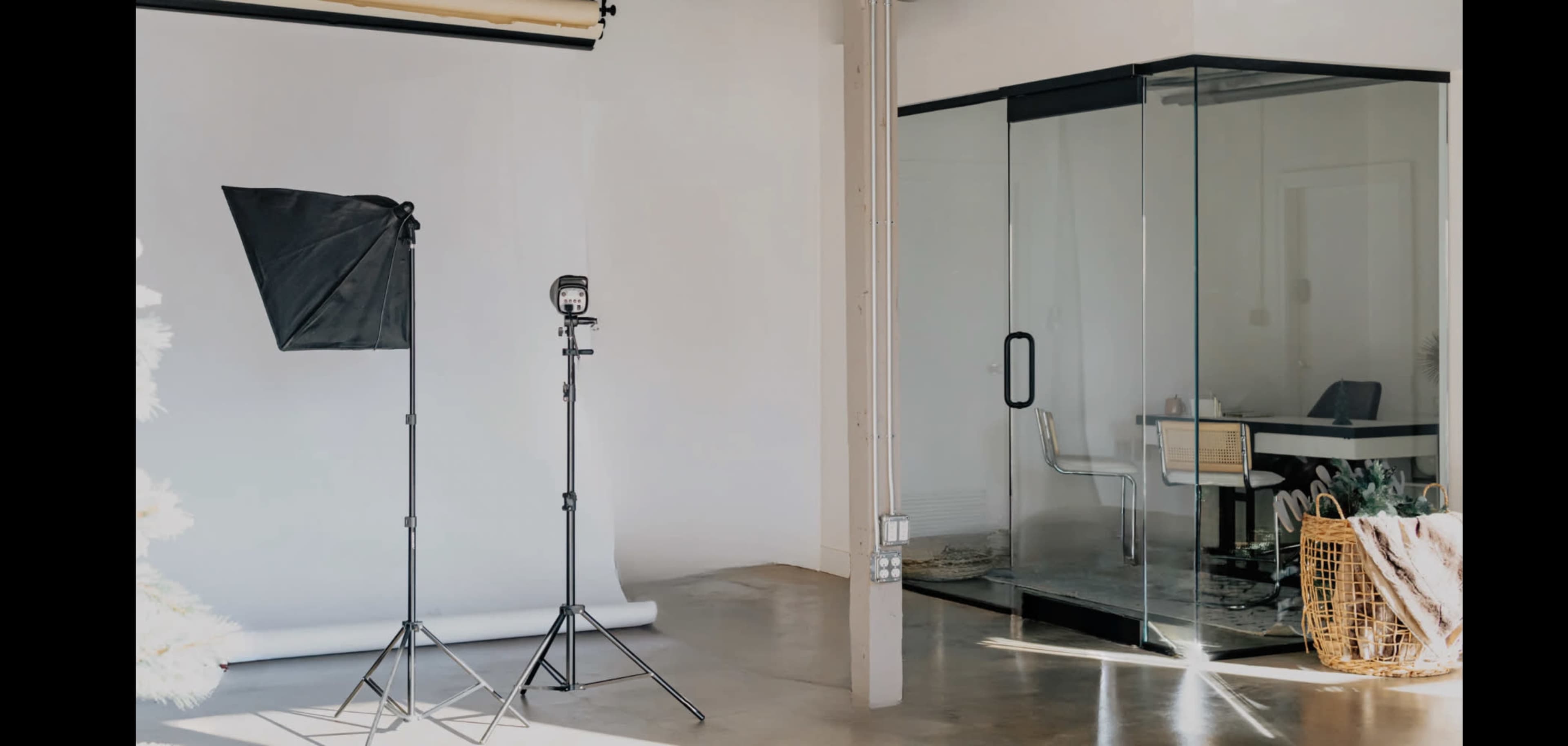 A photography studio with a black backdrop, a light stand, and a glass-enclosed workspace.