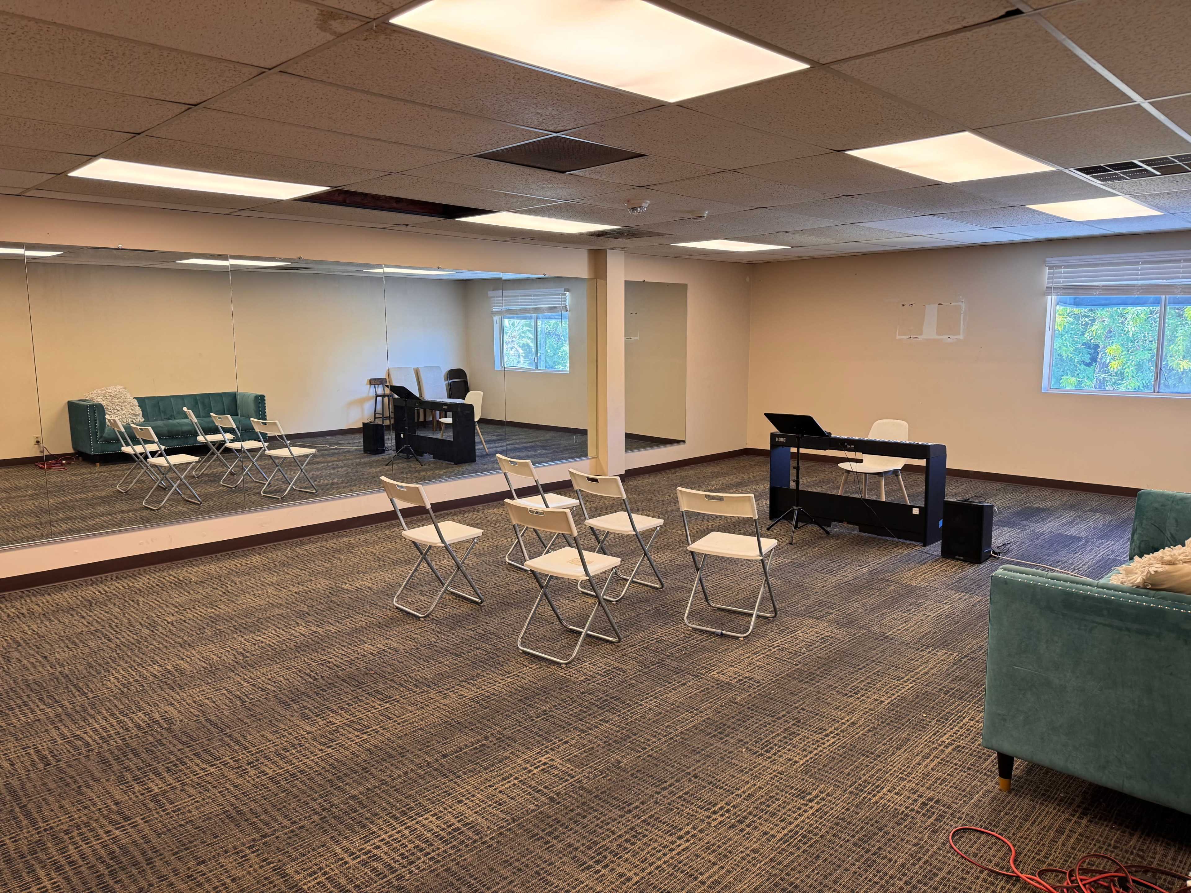 The image shows an empty room with a mirrored wall, several folding chairs arranged in a semicircle, and a desk with a laptop.
