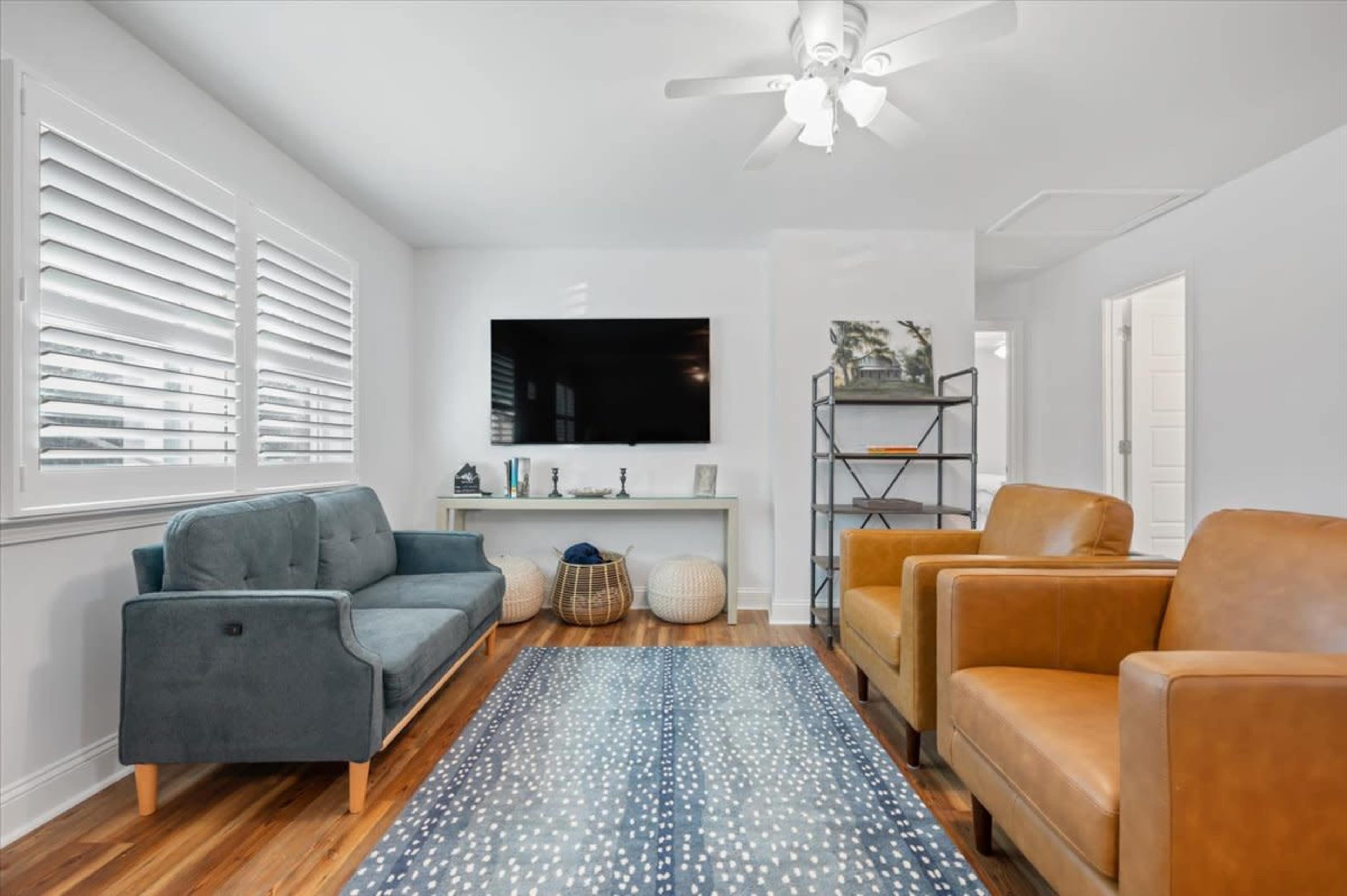 A well-lit living room featuring a gray sofa, two brown armchairs, a television mounted on the wall, and a decorative rug on a wooden floor.