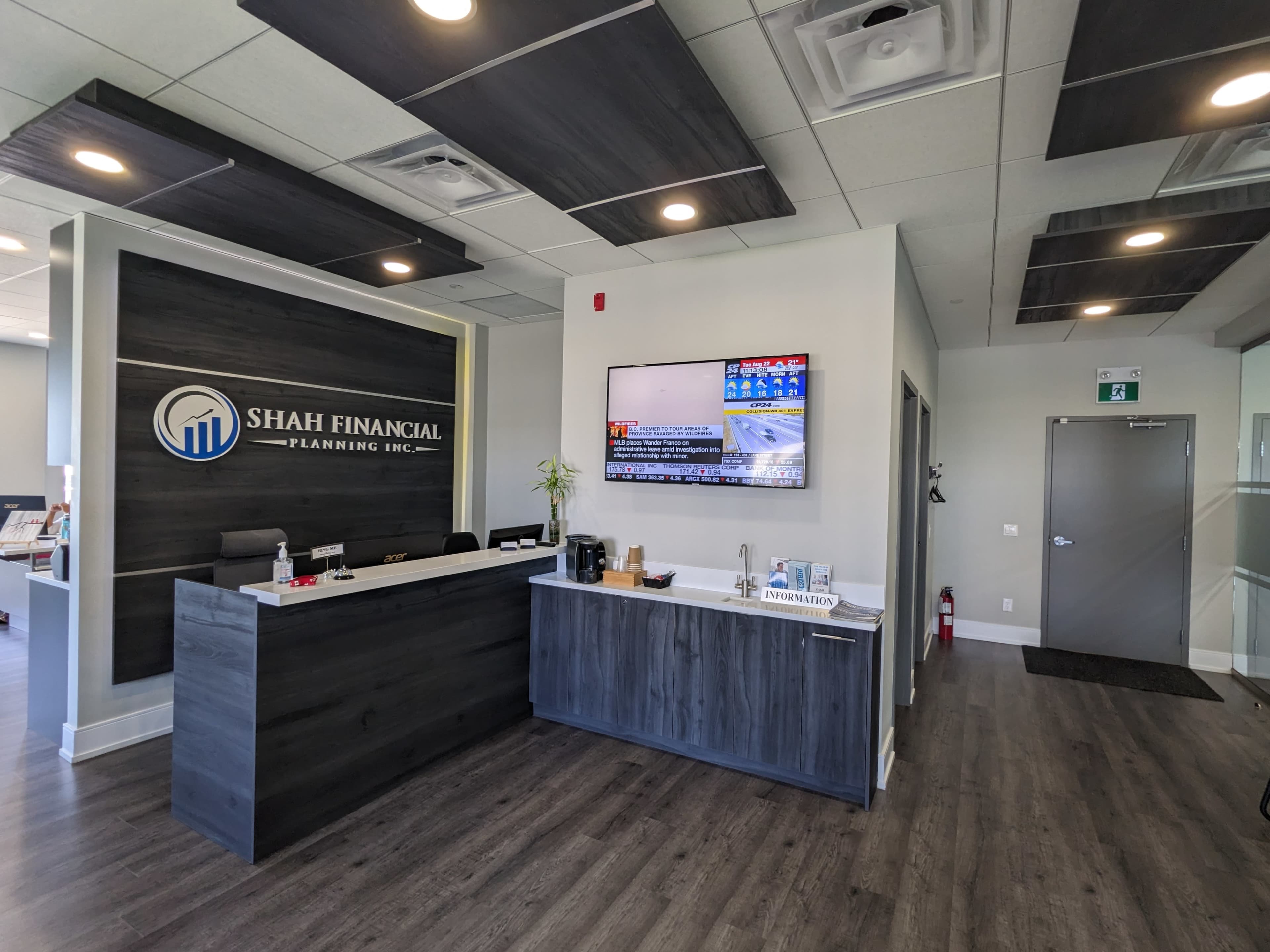 A modern reception area of Shah Financial Planning Inc., featuring a large logo on the wall, a flat-screen TV displaying news, and a sleek reception desk.