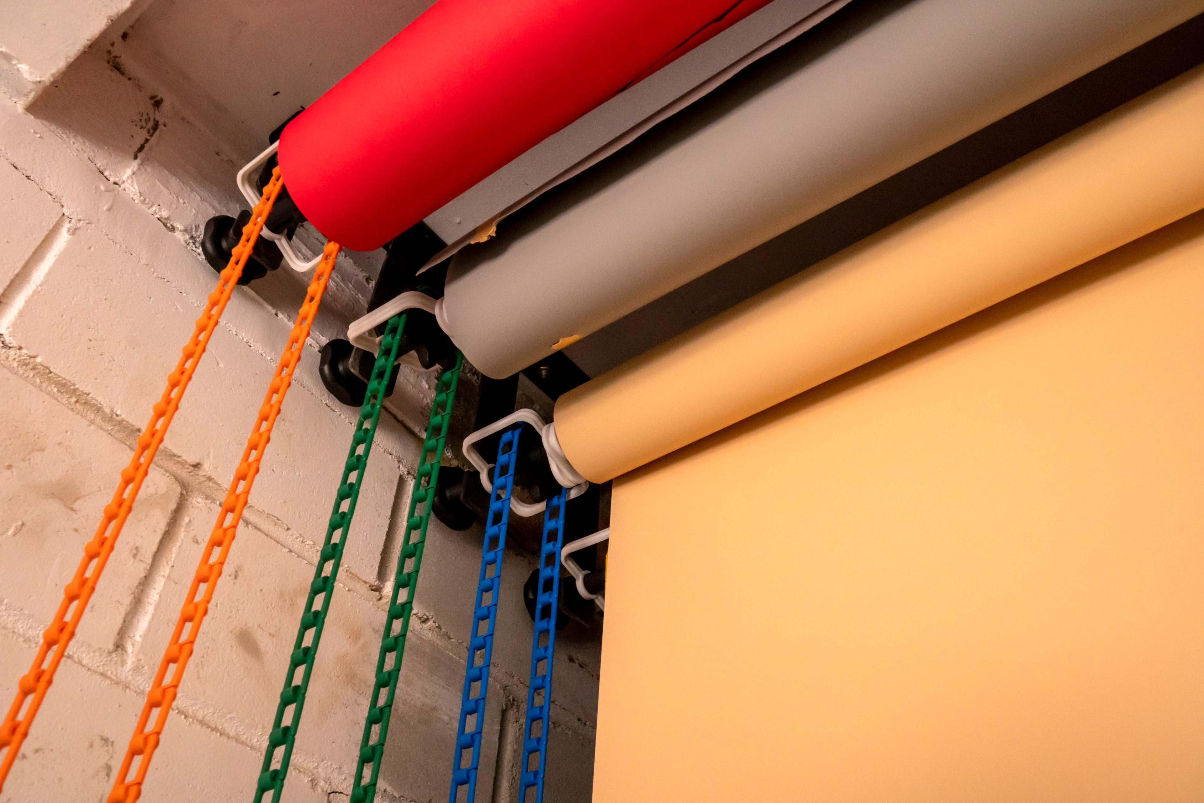 Several rolls of colored paper hanging from a ceiling, each connected to chains of various colors.