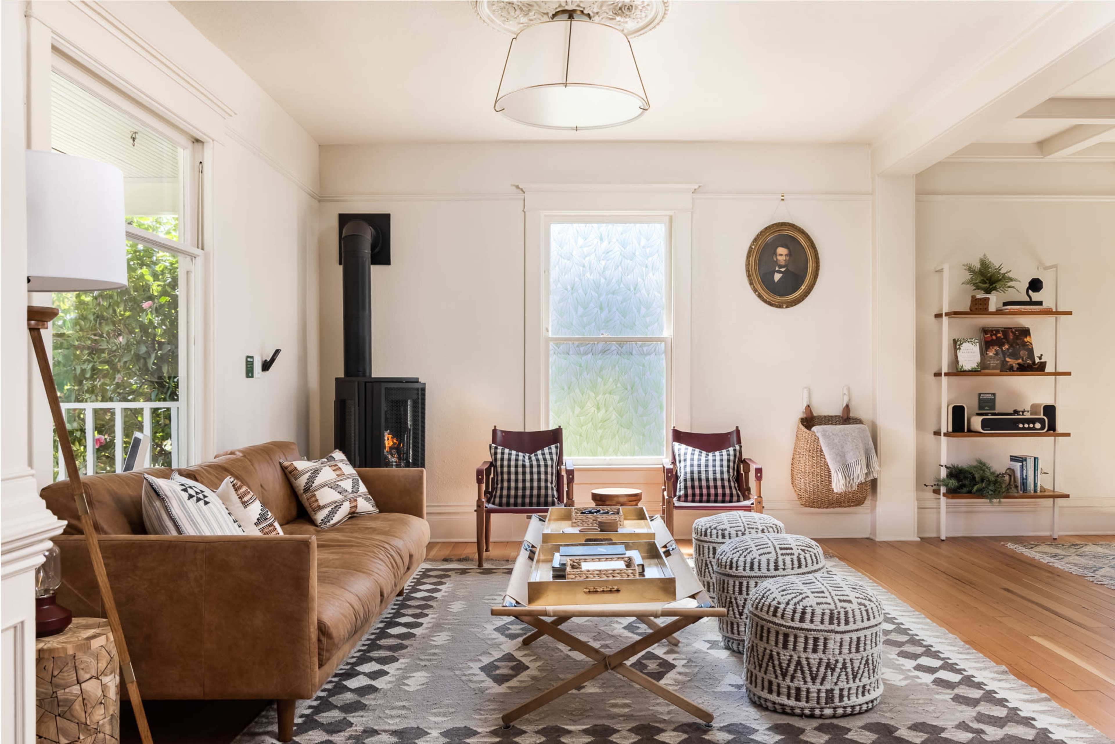 The living room features a brown leather sofa, two red chairs, a wooden coffee table, a decorative rug, and a wood-burning stove near a window.