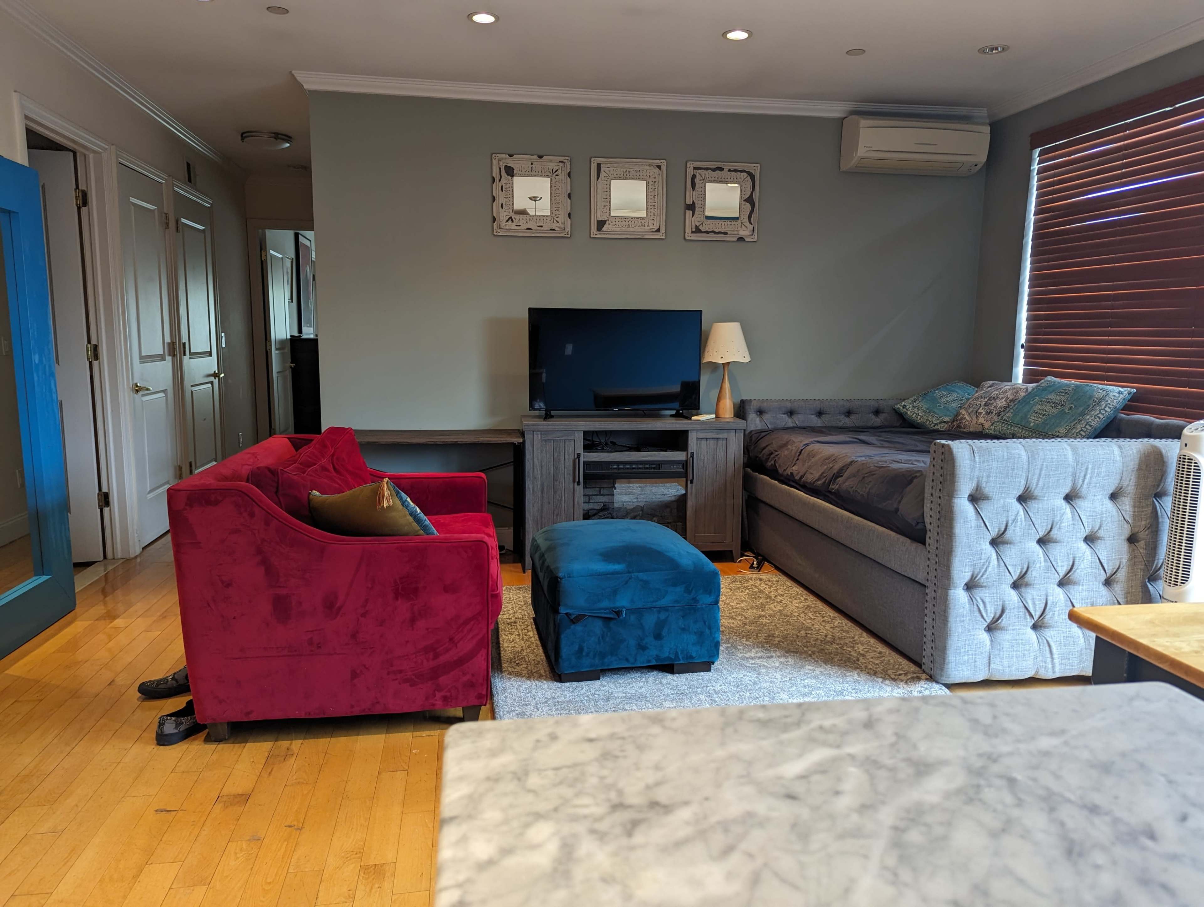 The living room features a red couch, a gray sectional sofa, a wooden TV stand with a television, and a small blue ottoman.