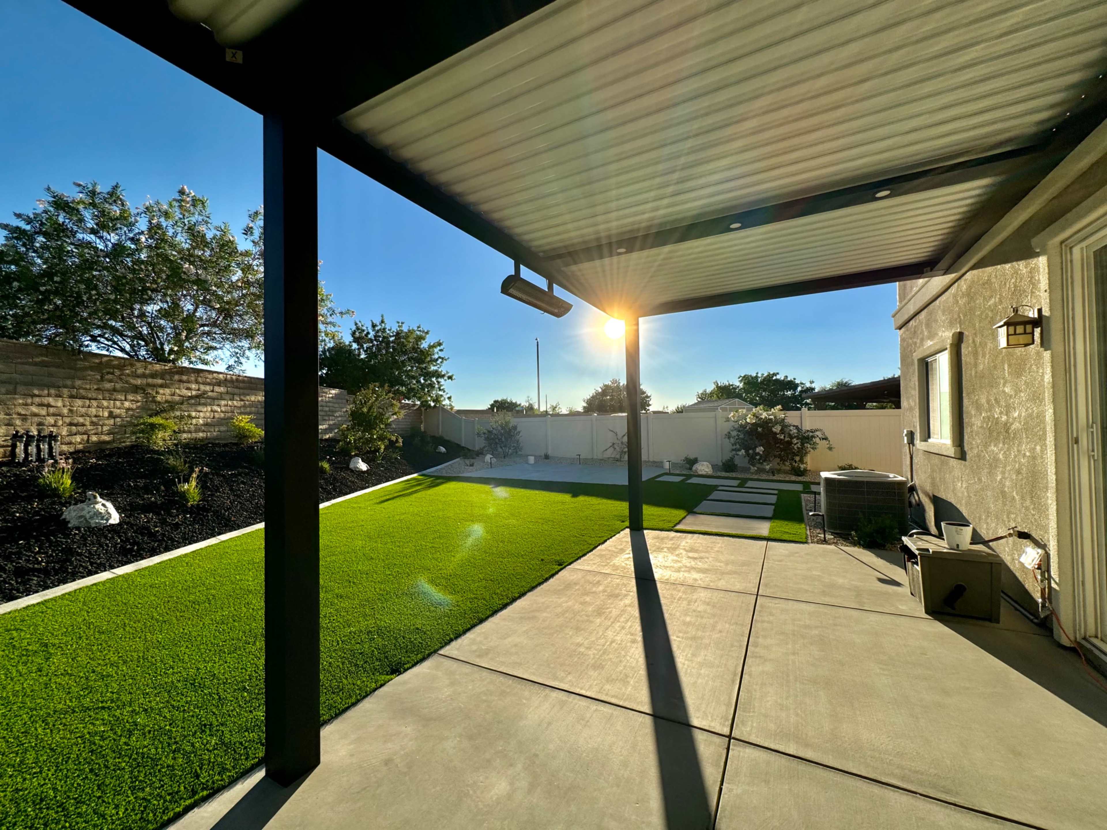 A backyard with artificial grass, a concrete patio, and a sun setting in the background.