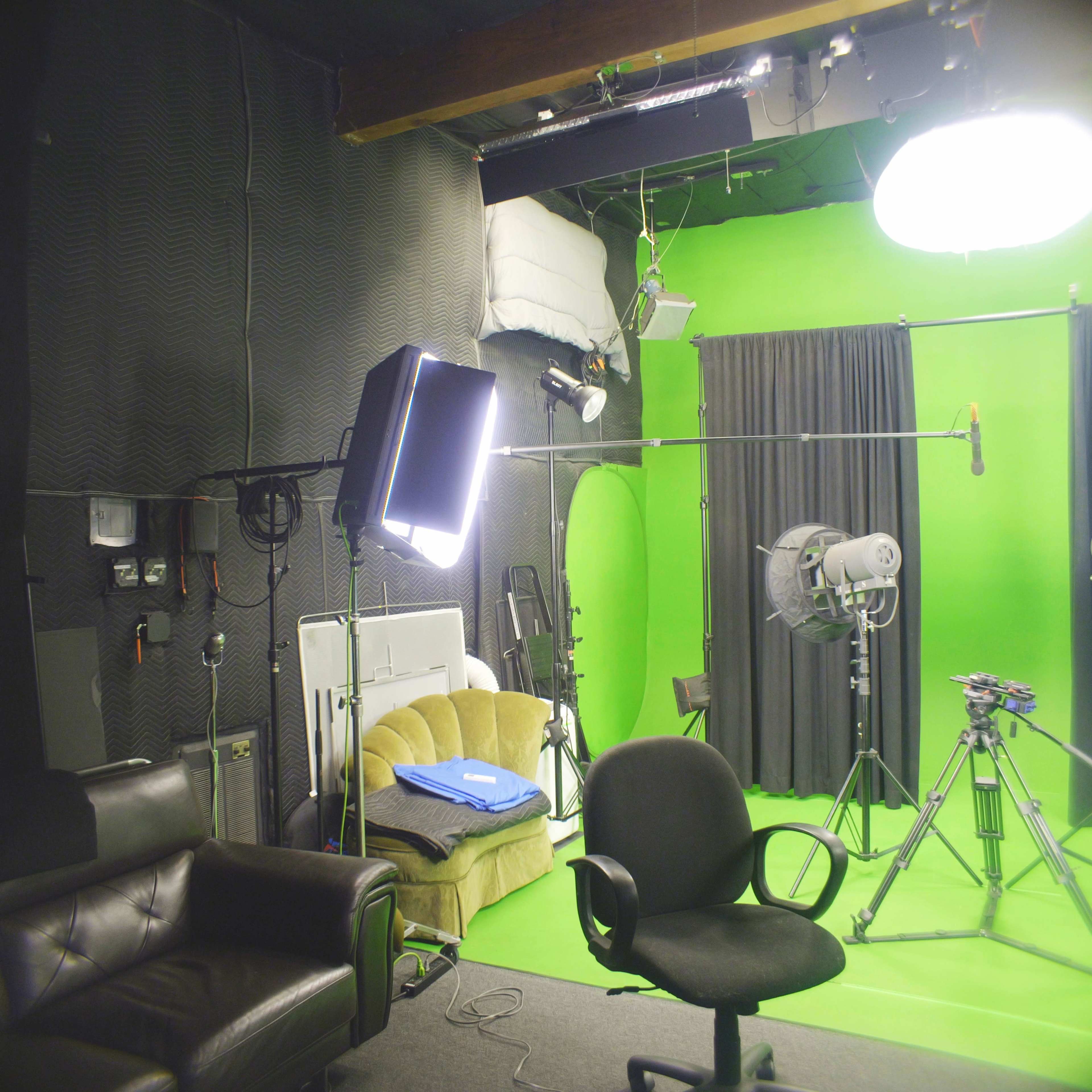 The image depicts a film studio with a green backdrop, lighting equipment, a black chair, and a couch.