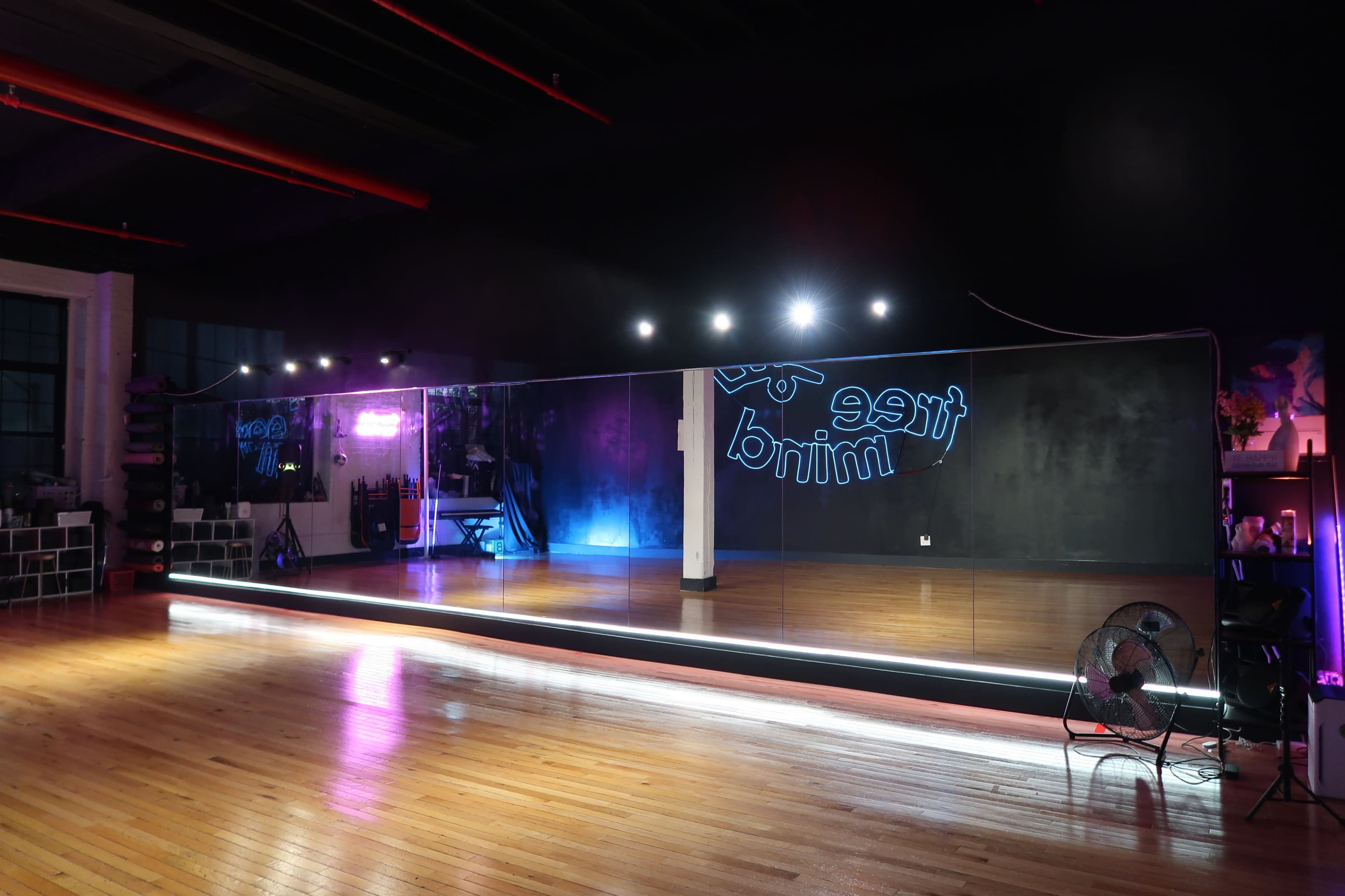 The image shows a dance studio featuring a large mirrored wall, wooden flooring, and ambient lighting.