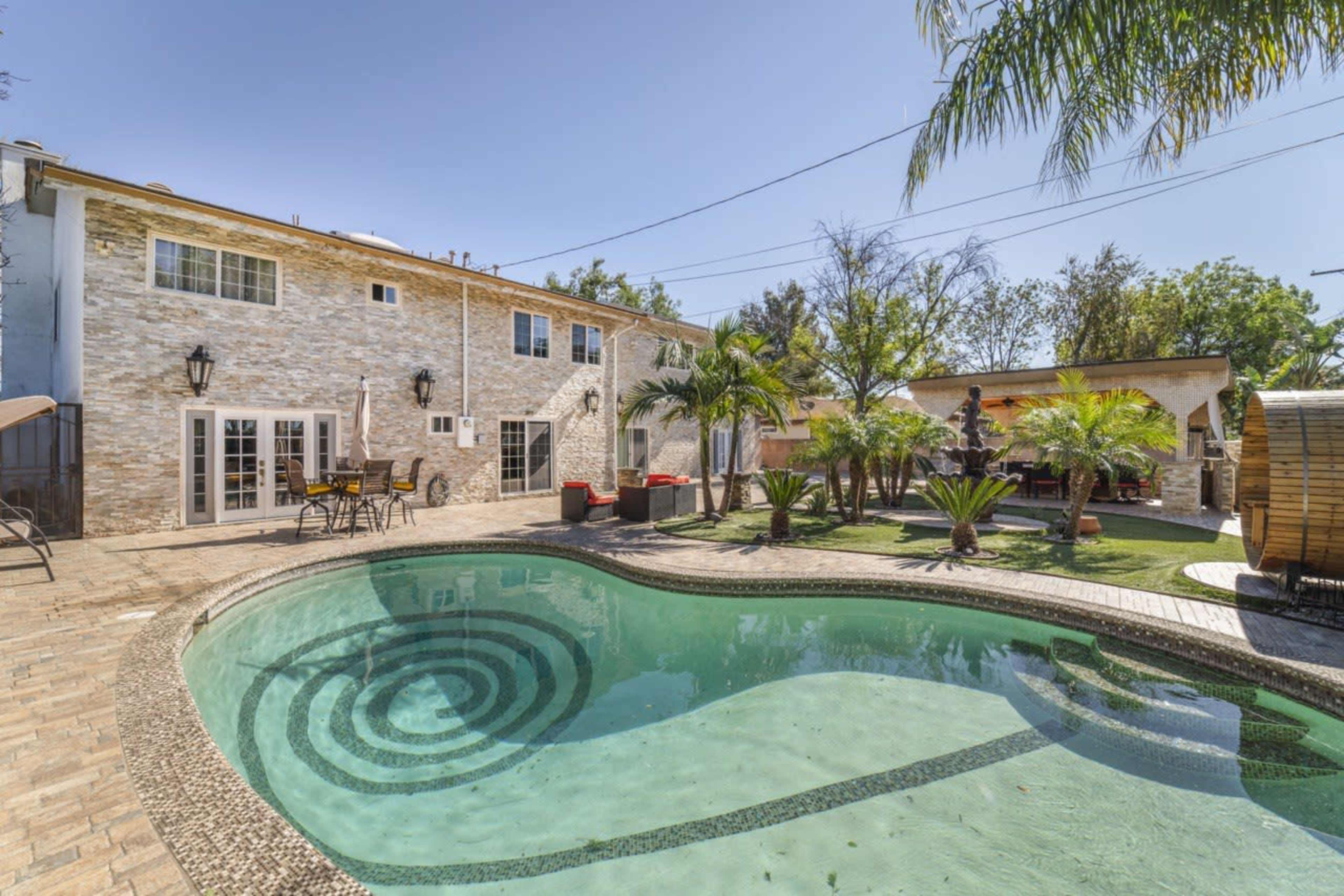A backyard with a swimming pool featuring a spiral pattern, surrounded by palm trees and patio furniture.