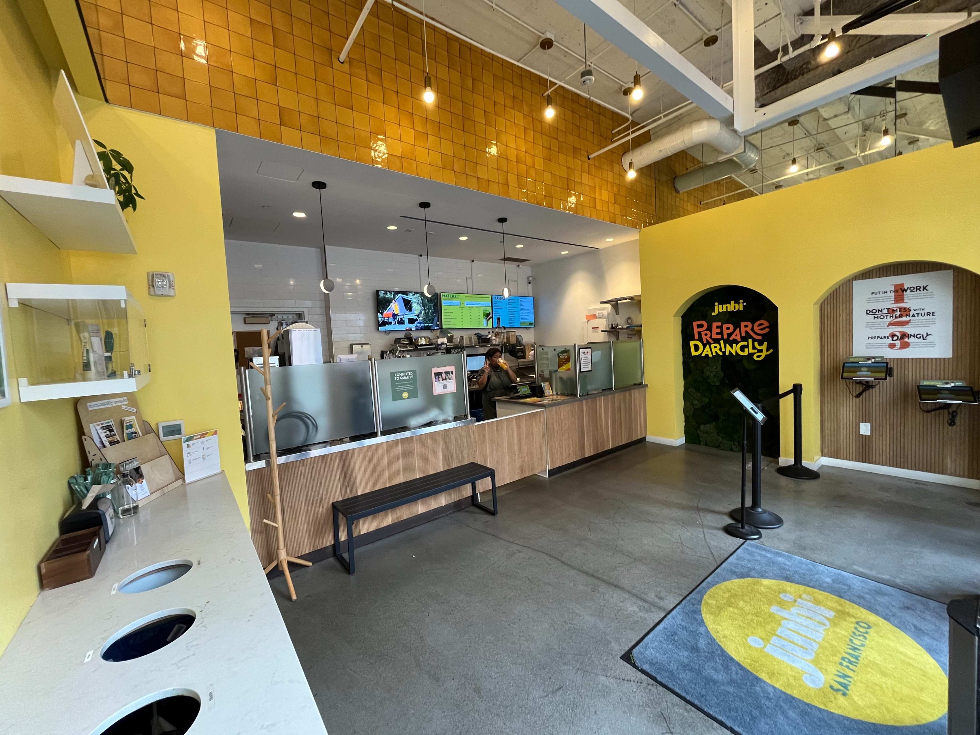 The image shows the interior of a brightly colored smoothie shop with a service counter, digital menu boards, and seating areas.